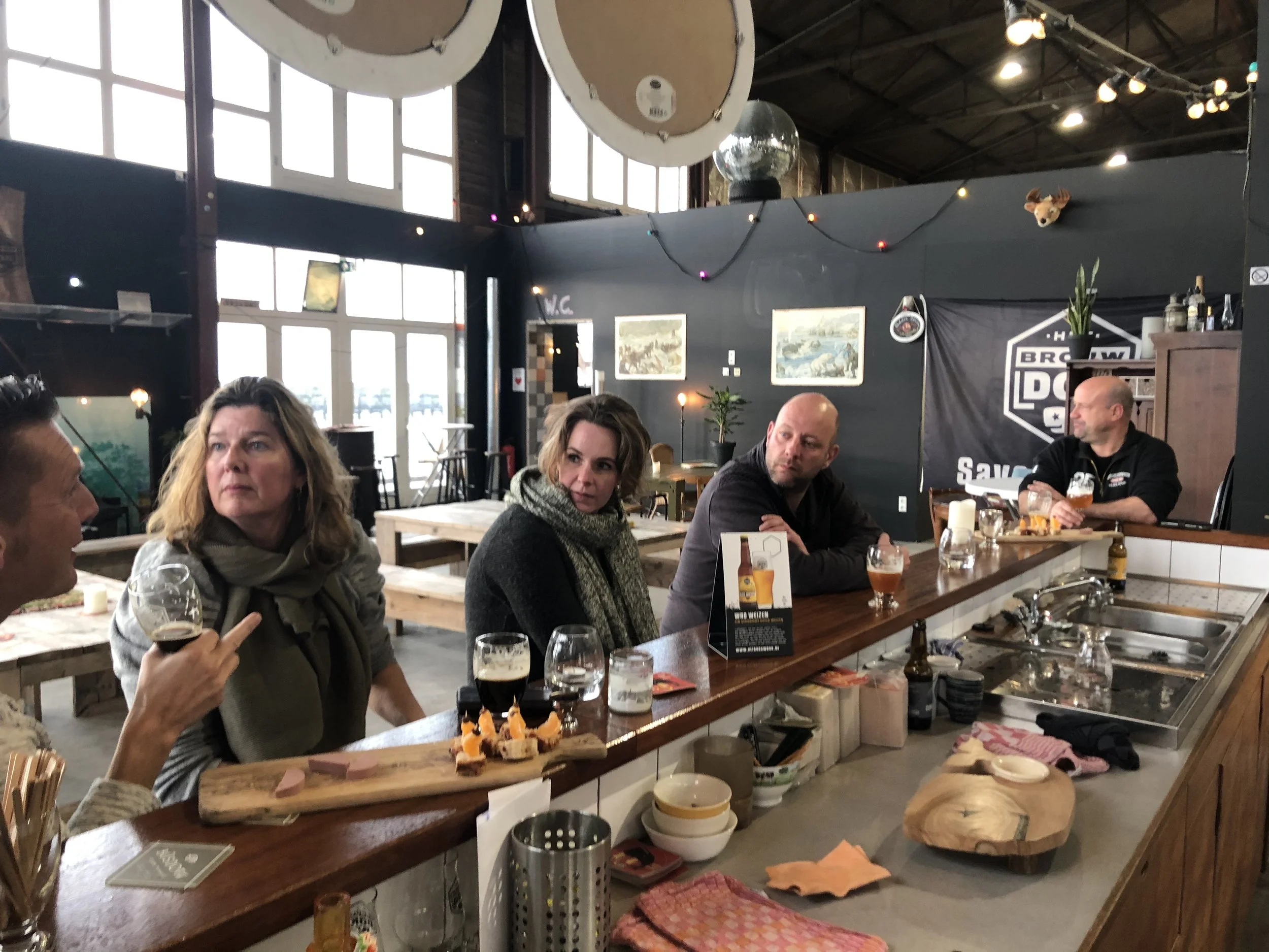 Gezellig restaurant met mensen die samen eten, decoratie met lampjes, schilderijen en een bar met drankjes.