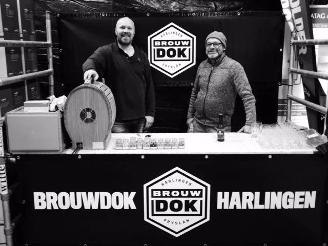 Twee mannen staan achter een kraam met branding, met banners die 'Brouwdok Harlingen' en 'Brouwdok Fryslân' zeggen.