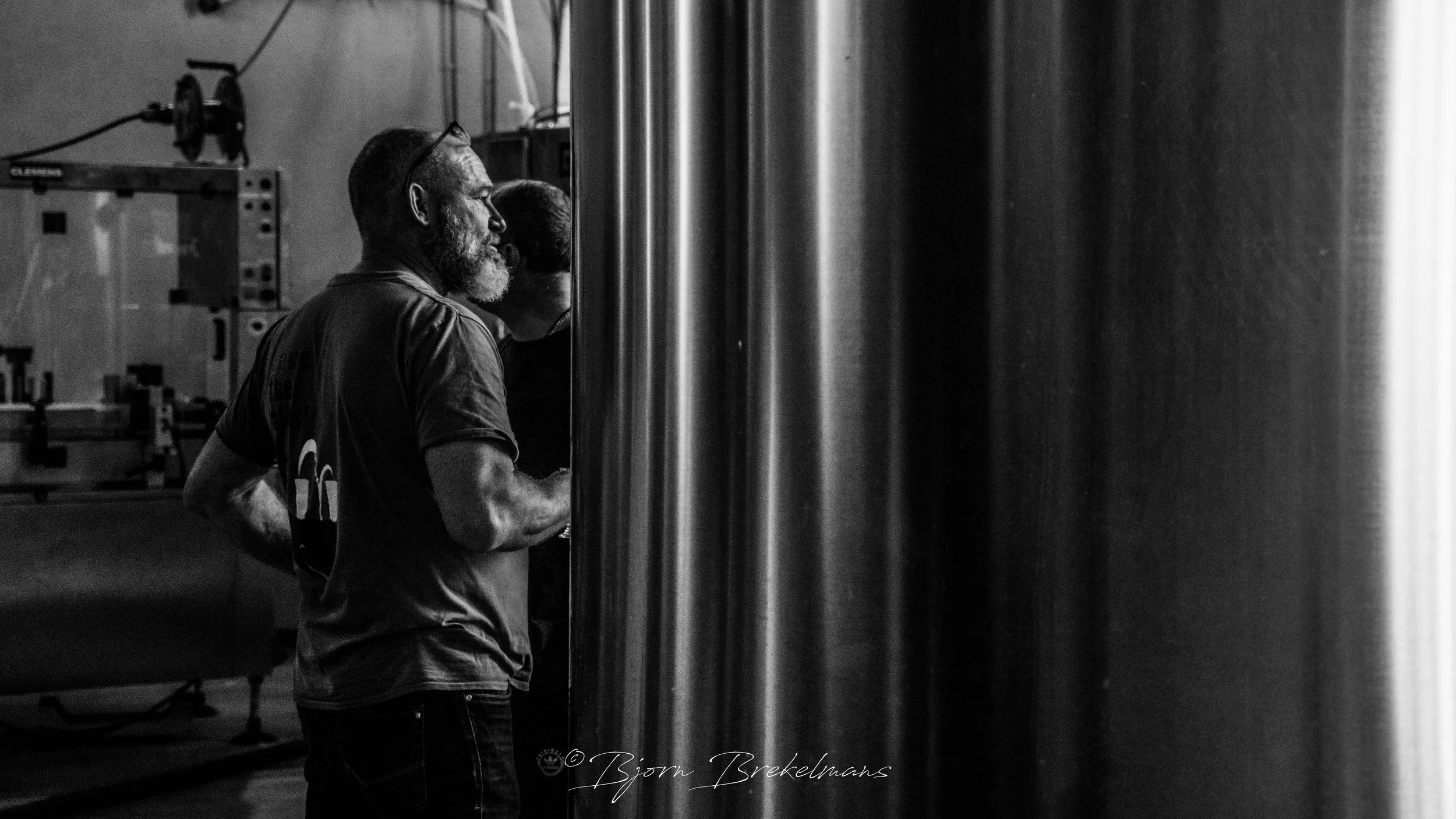 Twee mensen in een brouwerij of distilleerderij die naar een grote metalen vat of silo kijken.