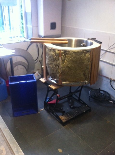 Een grote metalen kom of vat, mogelijk een bad of cadeau voor water, staat op een werkbank met gereedschap en elektrische kabels in de omgeving.