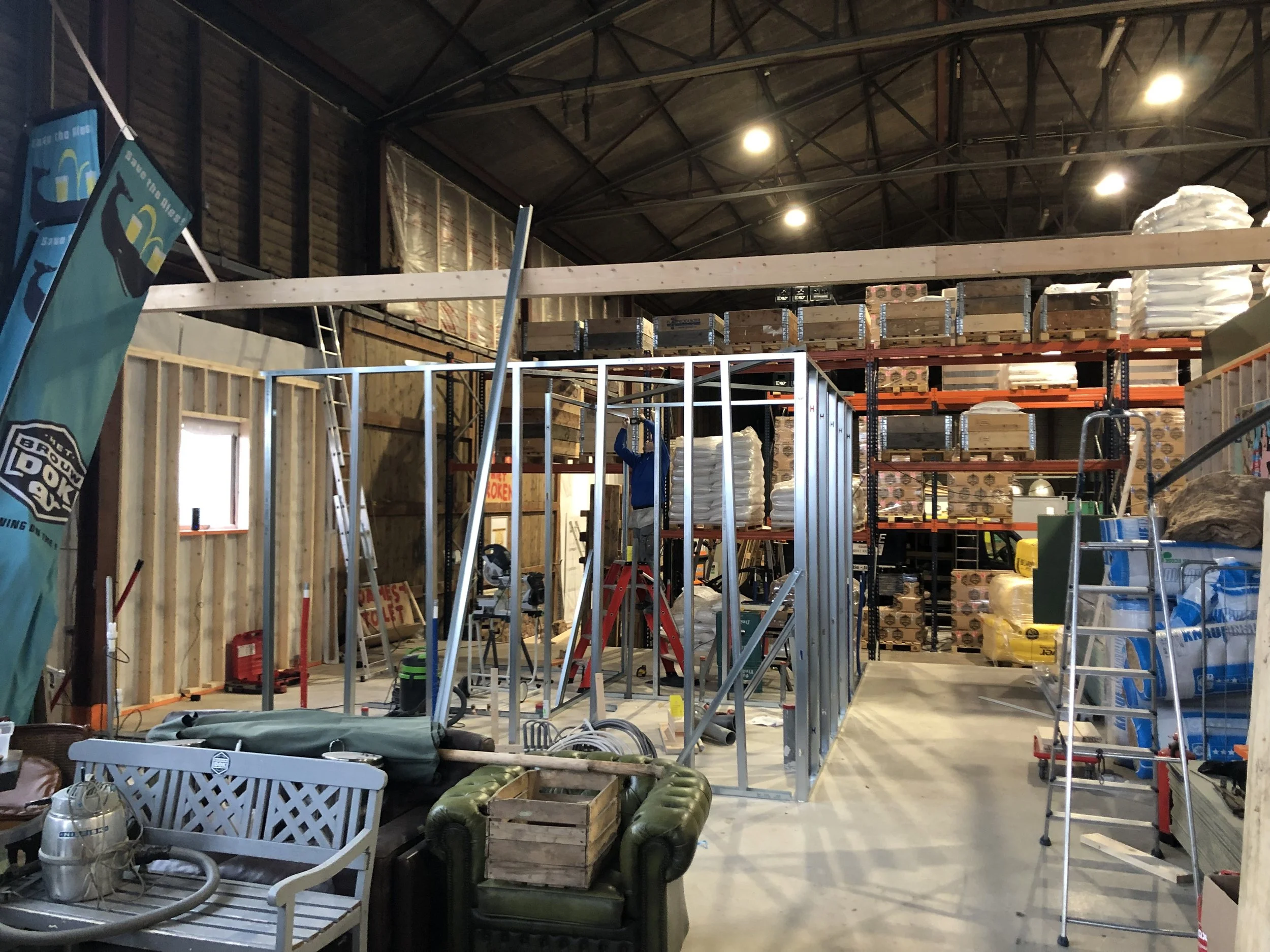 Binnenkant van een bouwplaats met gedefinieerde muren, meubels, ladders, en bouwmaterialen, klaar voor verdere constructie.
