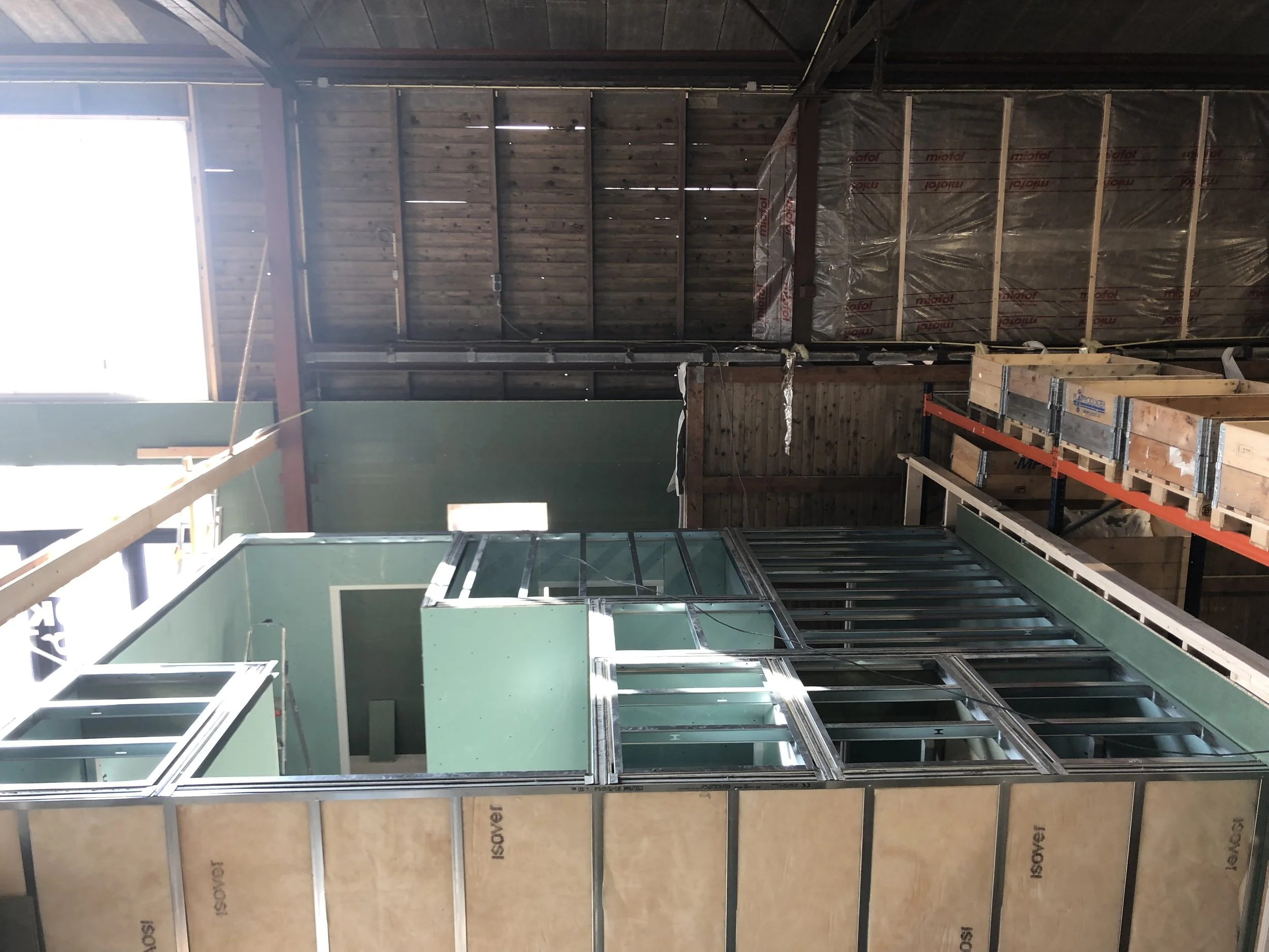 Binnenkant van een gebouw onder constructie met houten en metalen structuren, isolatiemateriaal en ramen.