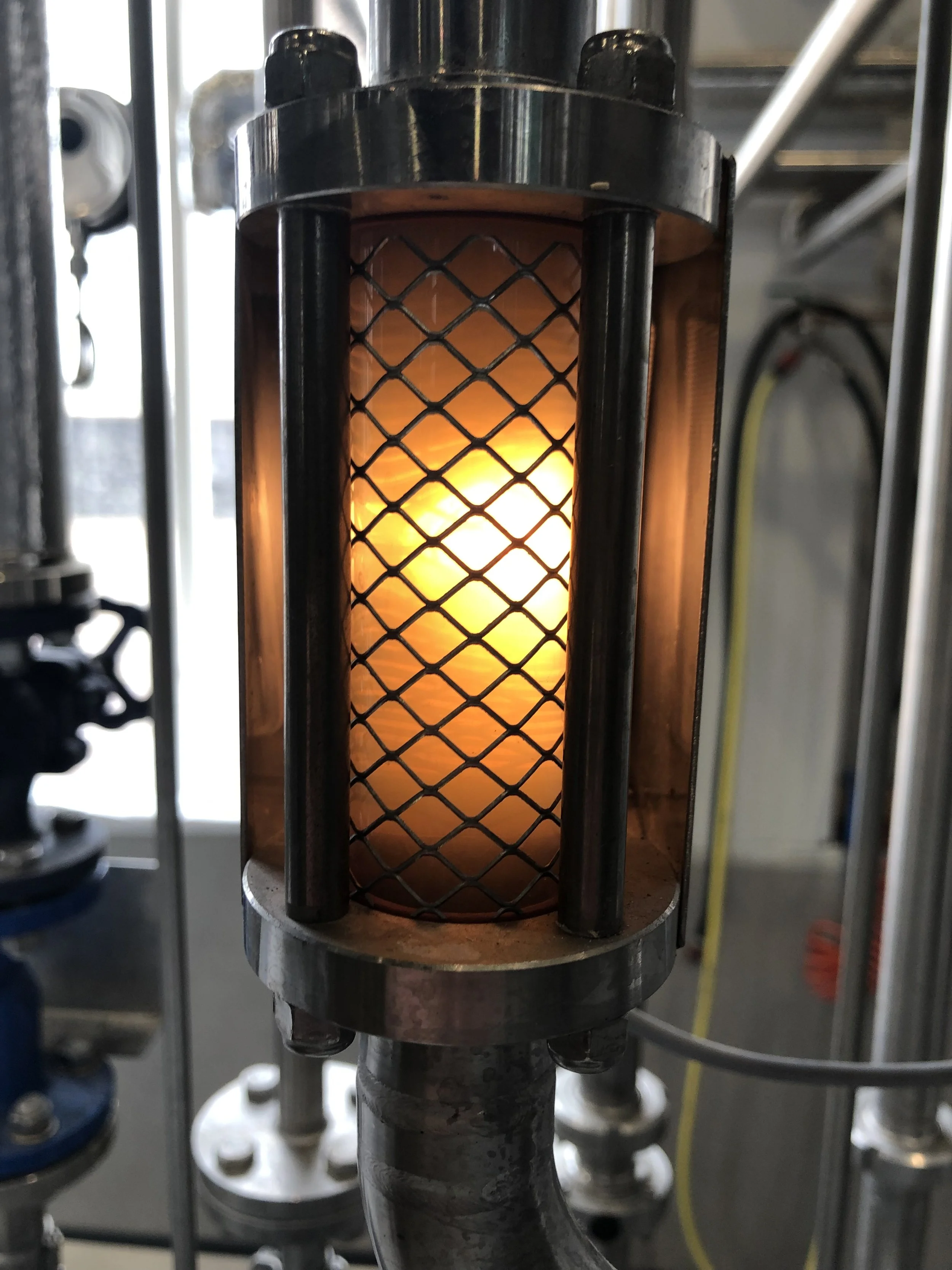Een metalen buis met een grafietmateriaaldelen, omgeven door een metalen raster, met een vlam die erachter zichtbaar is.