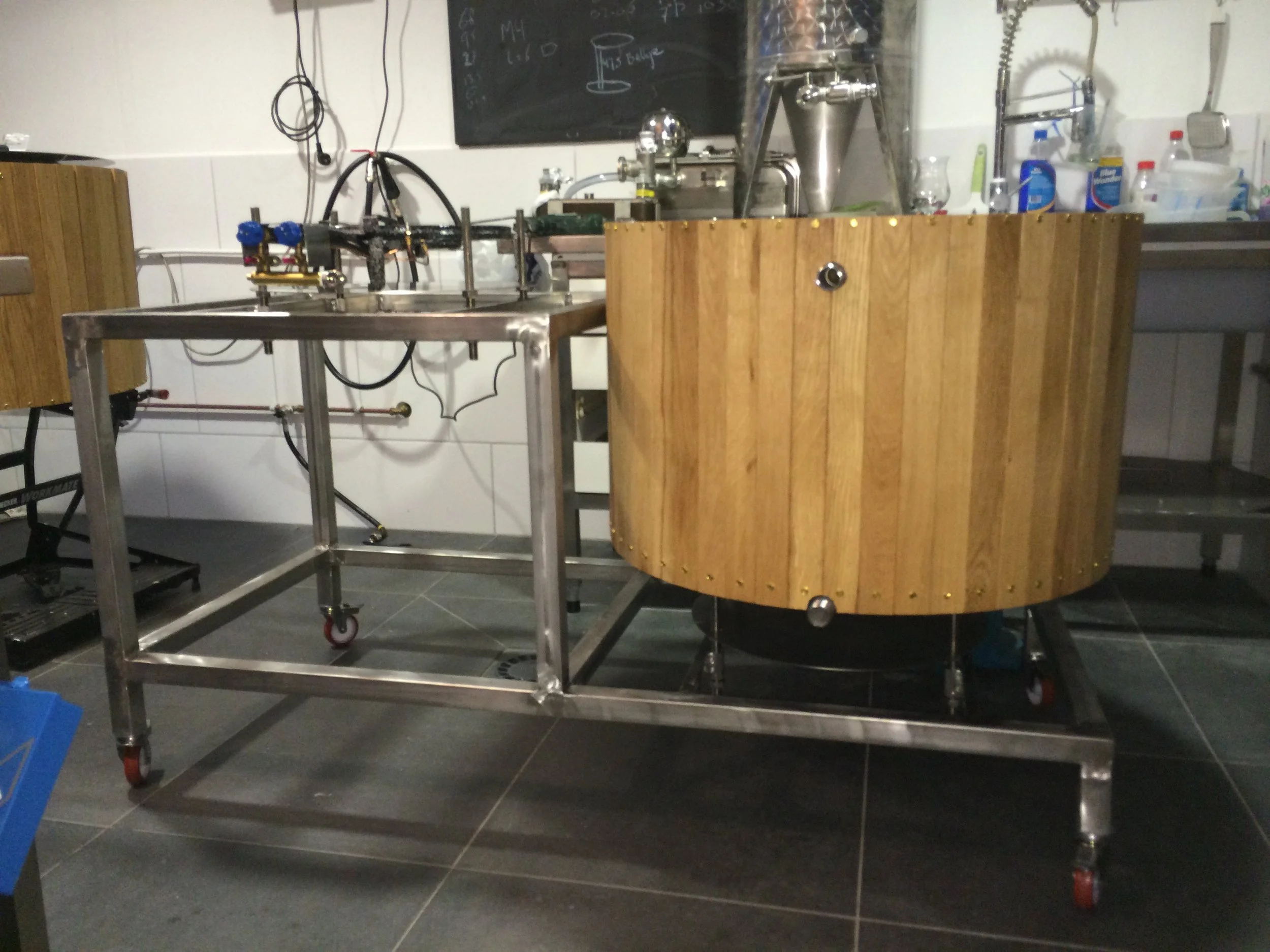 Een laboratoriumopstelling met een roestvrijstalen frame, een houten paneel en diverse schakelingen en apparatuur, inclusief een zwart bord met technische schetsen op de achtergrond.