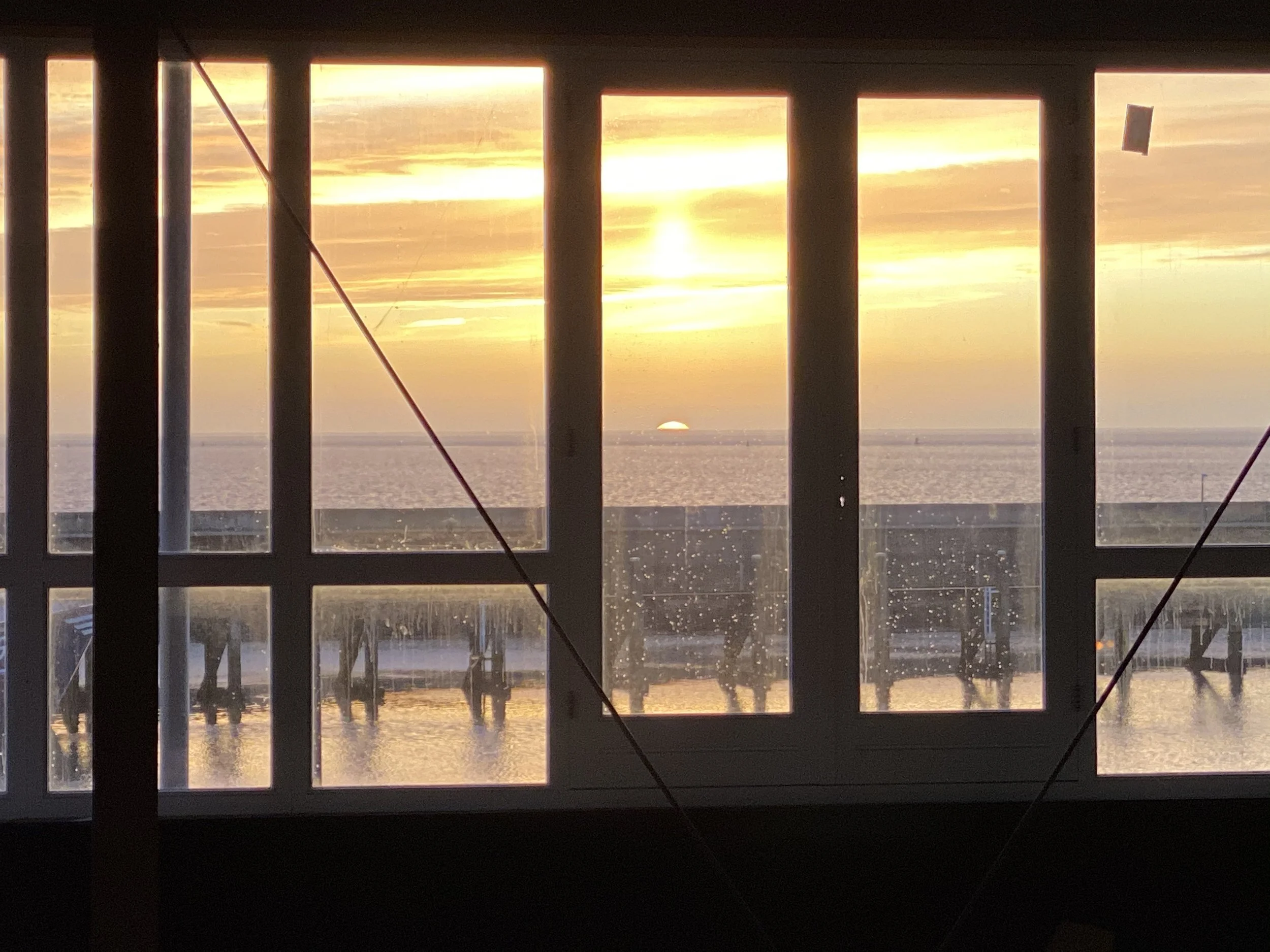 Zonsondergang zichtbaar door raam met vier panelen, uitzicht op water en een ponton.