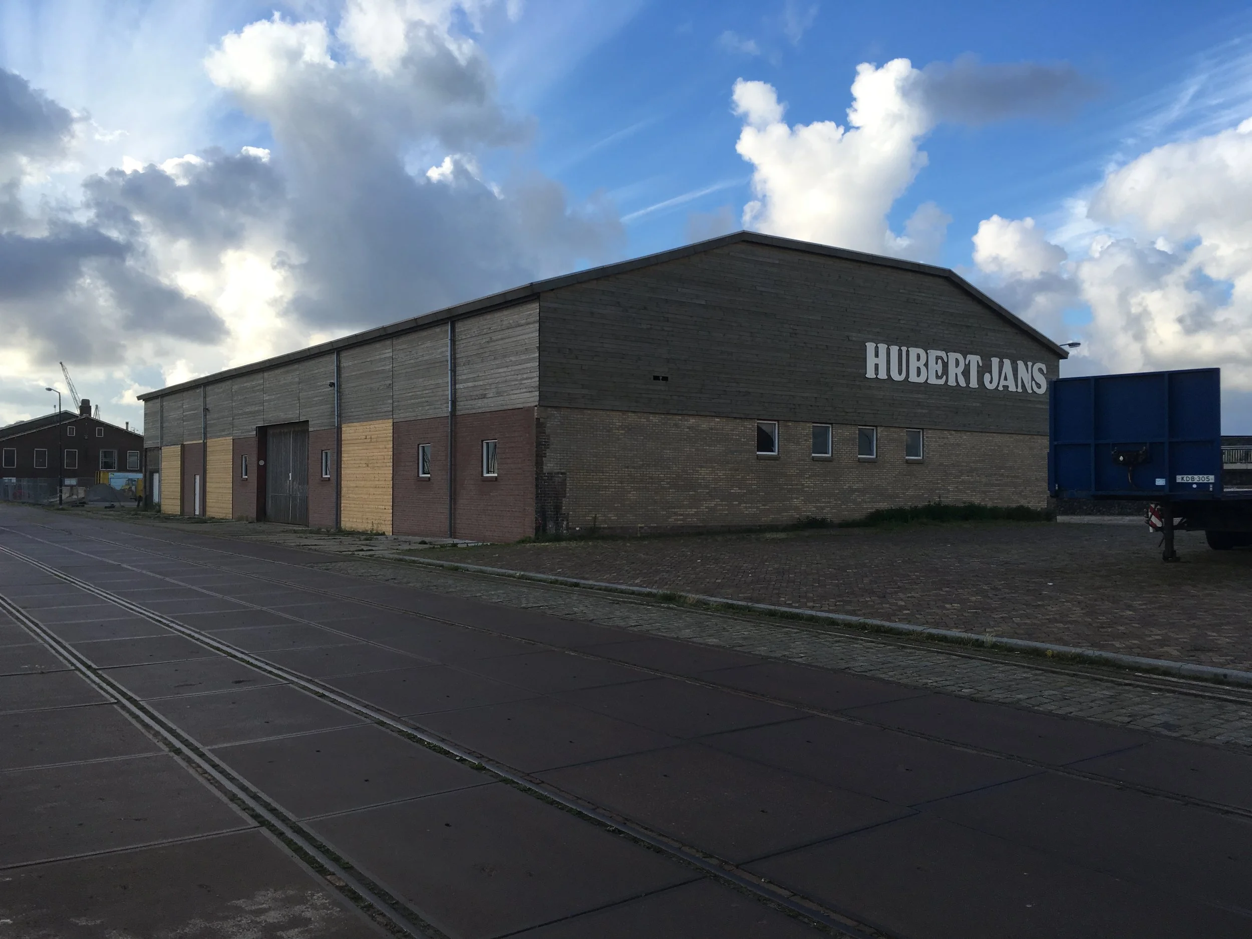 Een industrieel gebouw met de naam 'Hubert Jans' onder een bewolkte blauwe hemel.