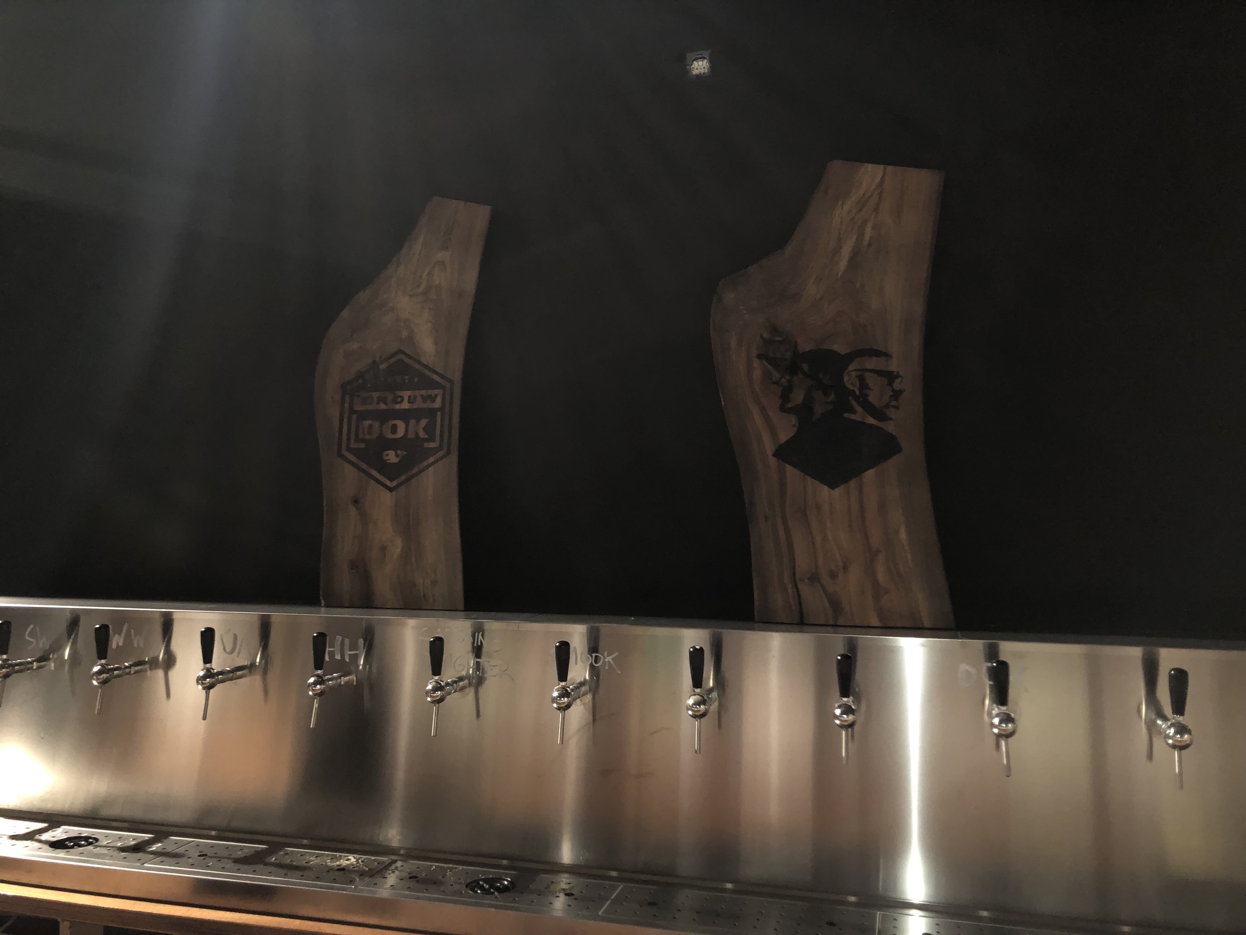 Een bar met meerdere tapkranen en houten planken met logo's, waaronder 'IDEO' en een afbeelding van een paard.