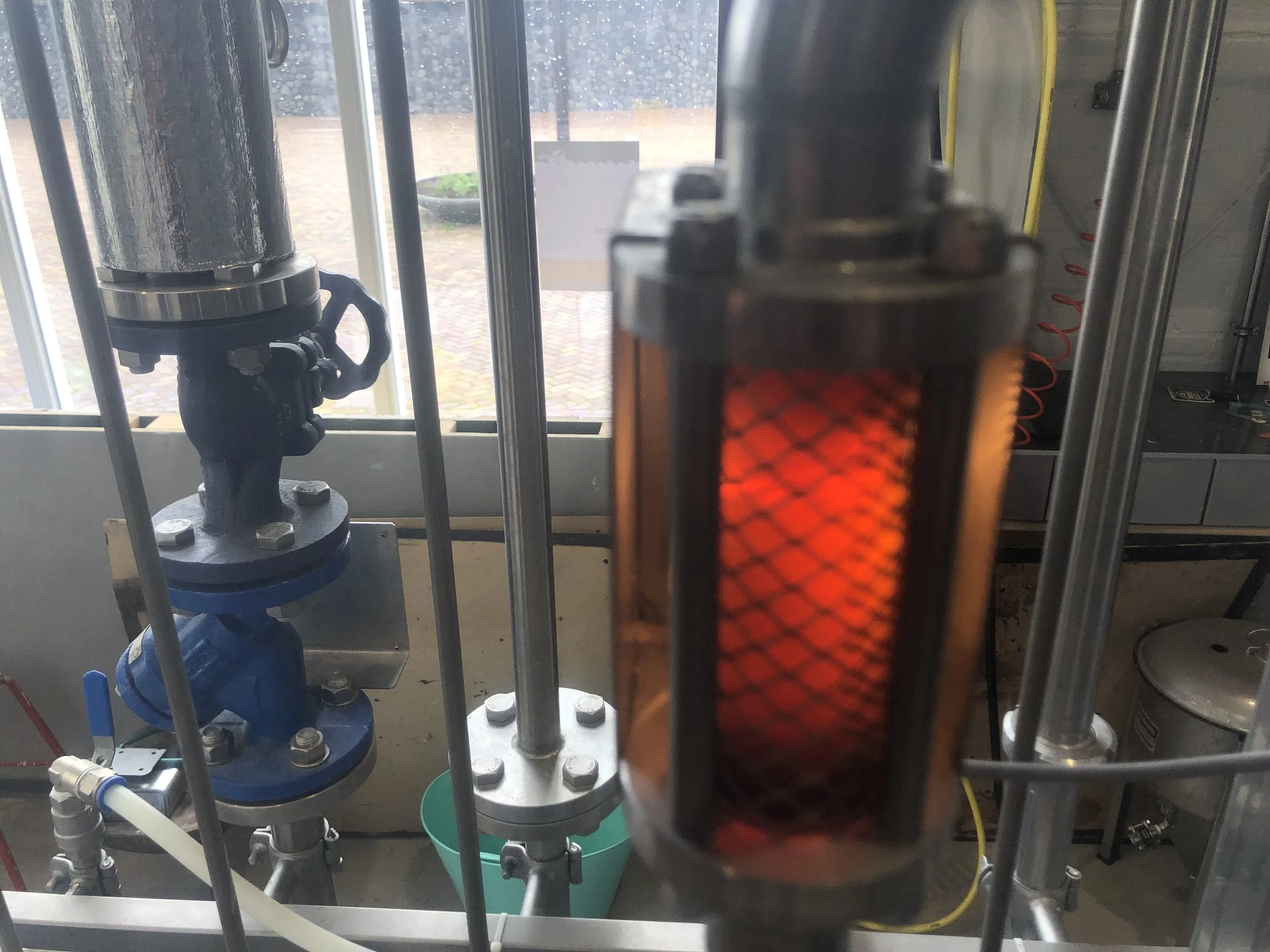 Binnenkant van een machine met metalen buizen, een verwarmingselement dat warm gloeid, en verschillende onderdelen zoals kleppen en bevestigingsbouten.