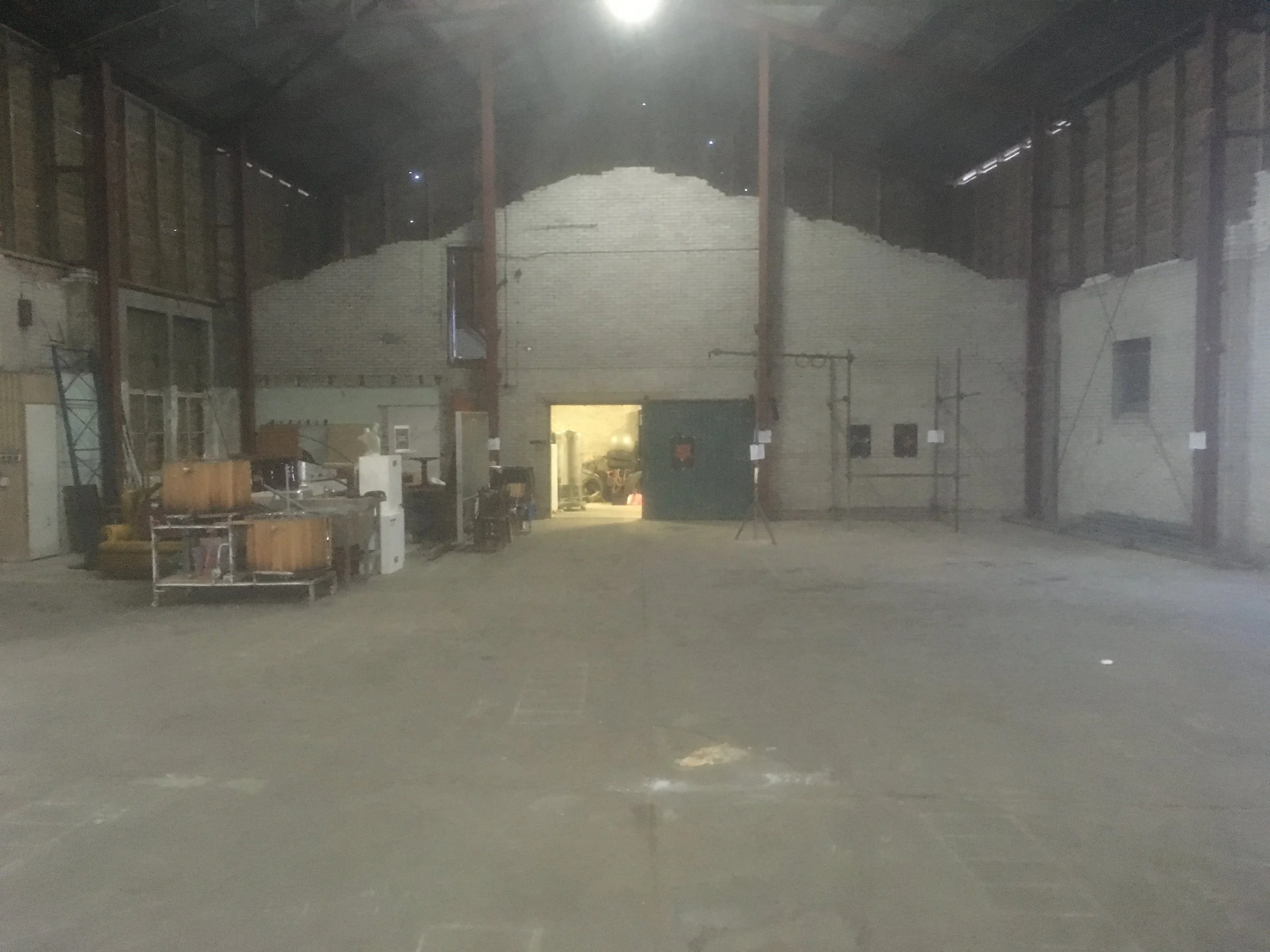 Een grote lege binnenruimte met een open deuropening en verschillende materialen en gereedschappen op de vloer, mogelijk een bouwplaats of opslagruimte.