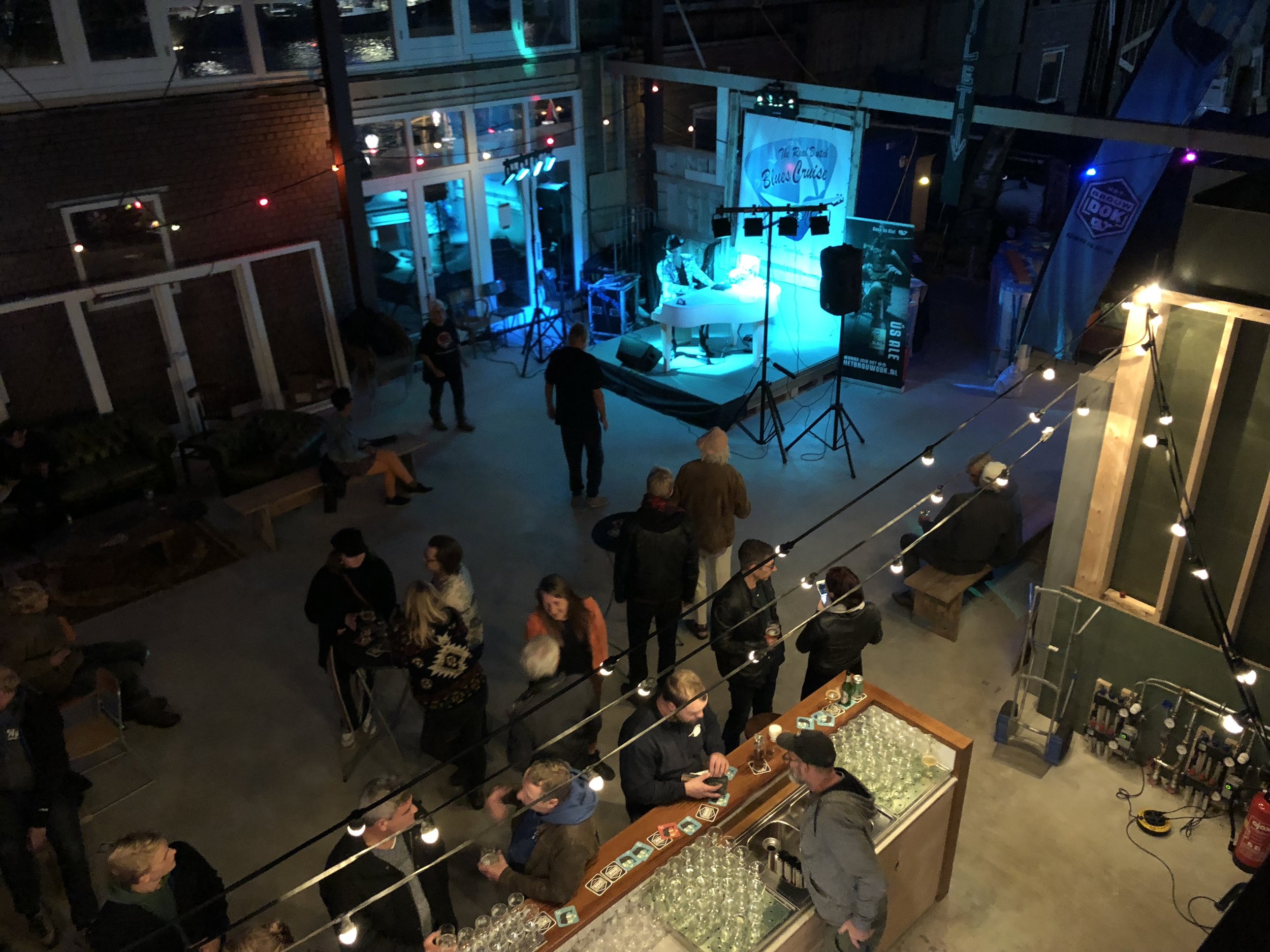 Een levendige overheidsfeestzaal met mensen die genieten, een podium met muzikanten en kleurrijke feestverlichting.