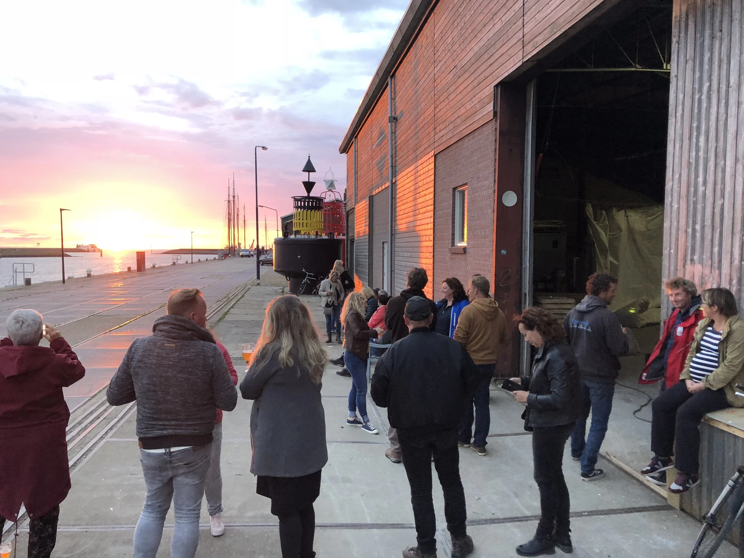 Mensen die in groep samen op een pier bij de haven staan en uitkijken naar de zonsondergang boven de rivier.