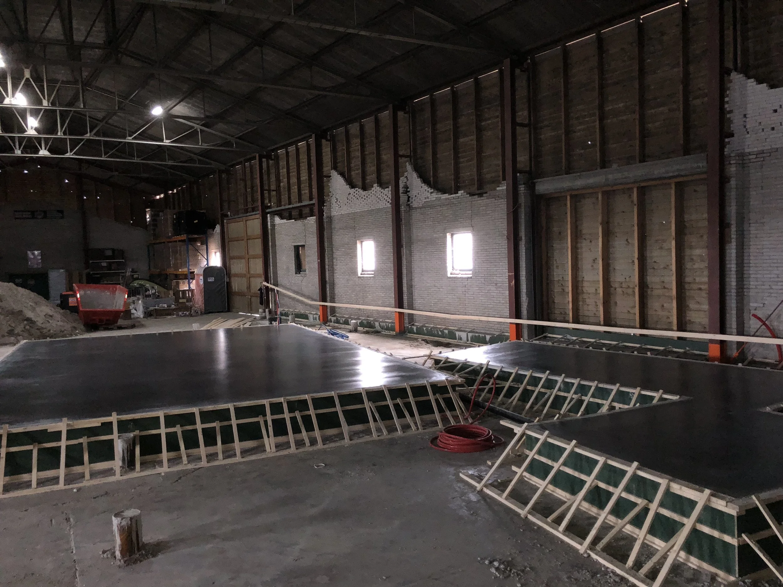 Binnenaanzicht van een gebouw onder constructie, met bakvormen en bouwmaterialen, muren en ramen die nog afgemaakt moeten worden.