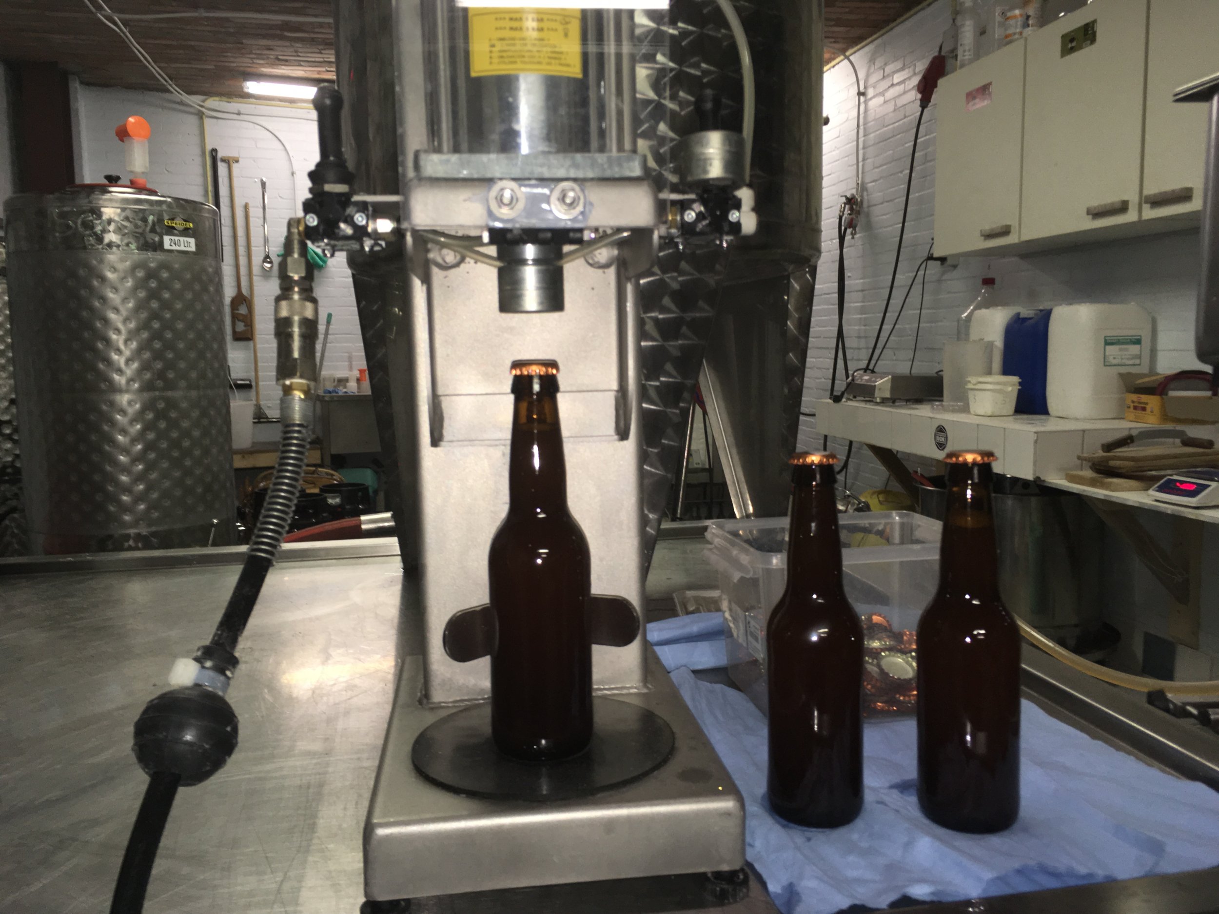 Een industrieel apparaat dat bierflessen afvult, met vier bierflesjes in de voorgrond.
