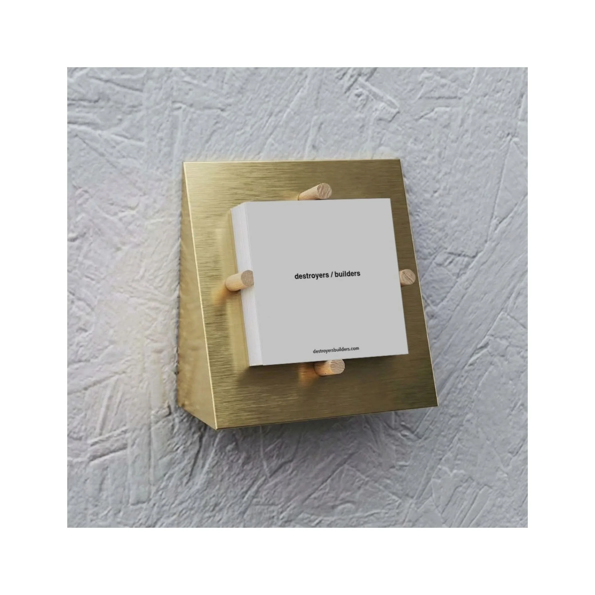 Close-up view of a mirror with a gold-colored wooden frame, positioned on a textured white surface with a label reading "destroyers/builders" and a website URL.
