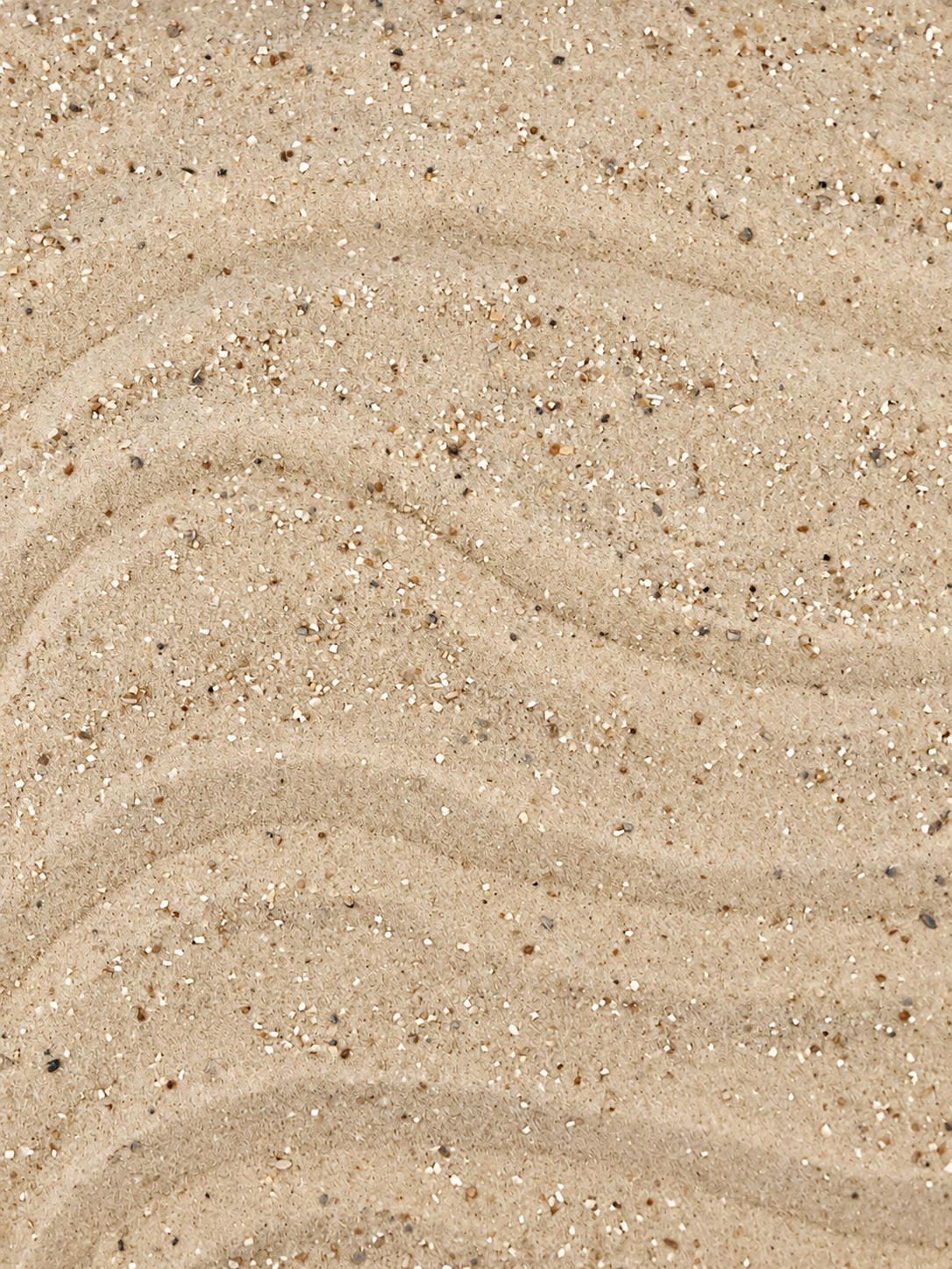 Sand mit kleinen, farbigen Steinchen und leichten Wellenmuster.