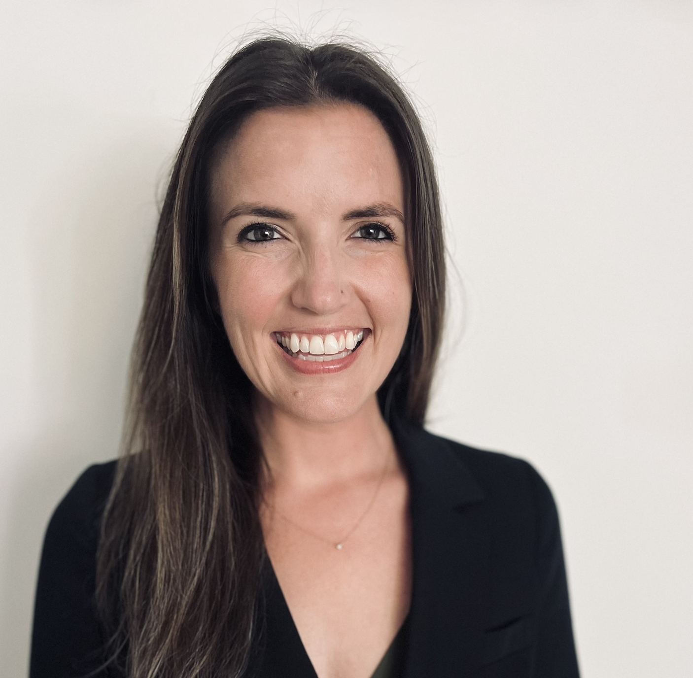 A woman with long dark hair, smiling, wearing a black top against a plain white background.