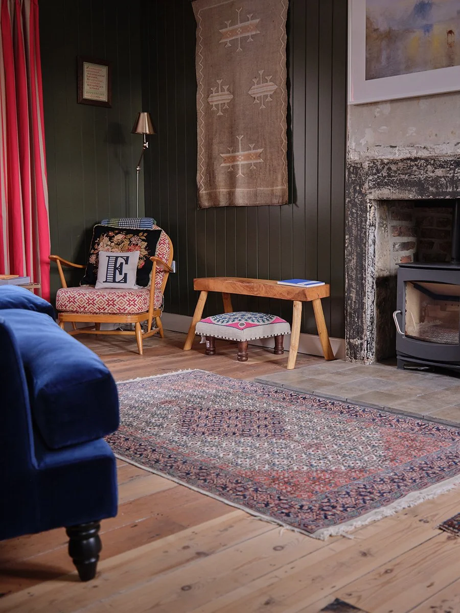 Eclectic living room with patterned area rug, floral armchair, wood bench, blue sofa, wall tapestry, and stone fireplace