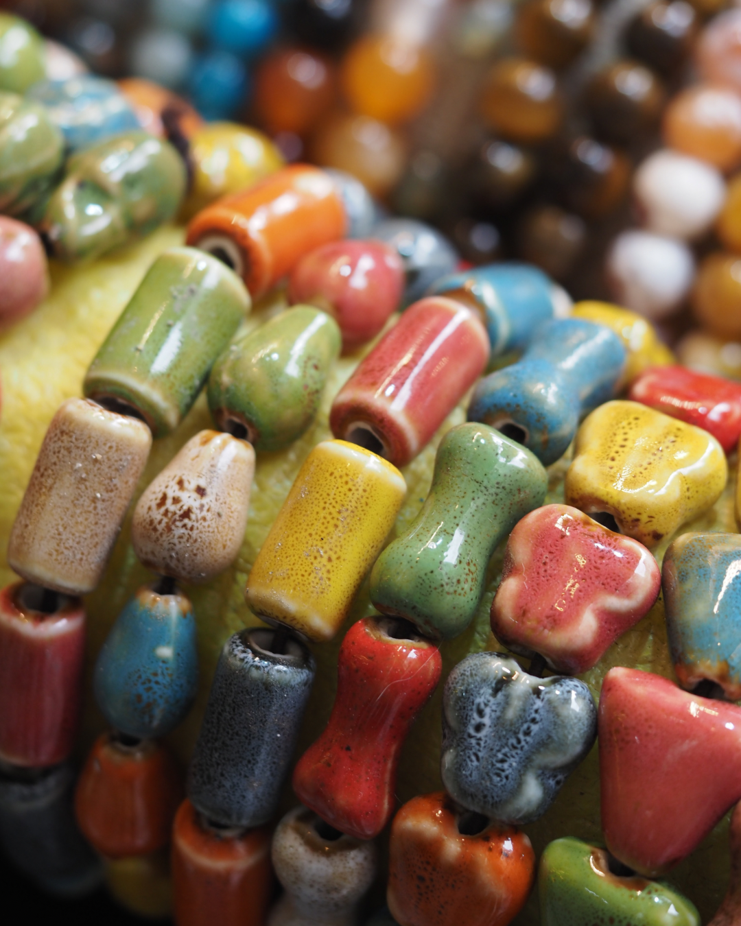 Bunte Keramikperlen in verschiedenen Farben und Mustern, aufgereiht auf einer Oberfläche.