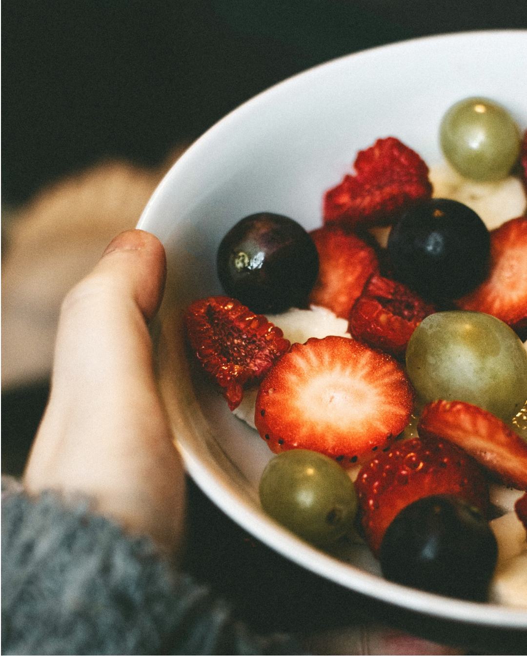 Hand hält Schüssel mit Erdbeeren, Heidelbeeren und grünen Weintrauben.