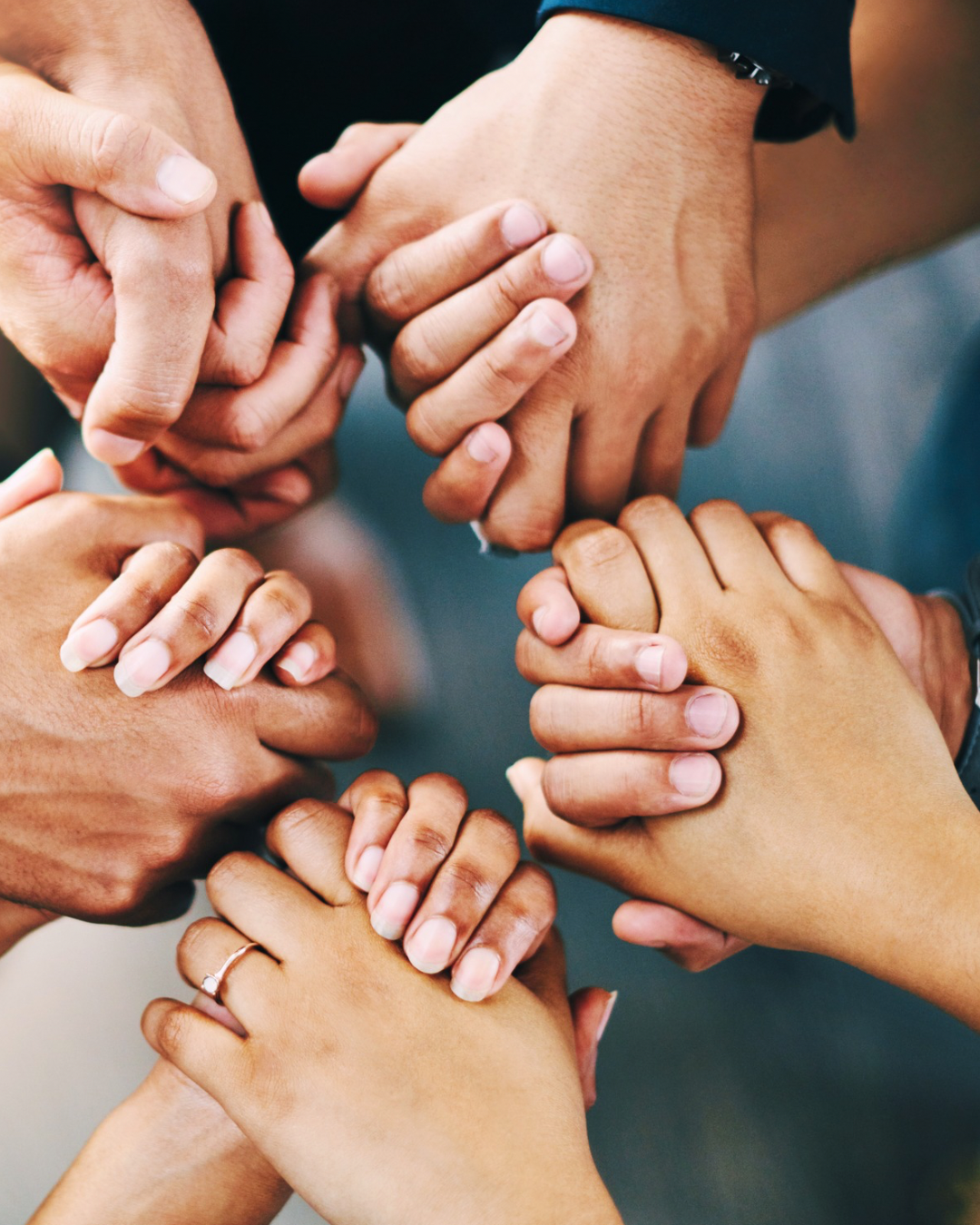 Mehrere Hände verschiedener Menschen greifen sich in der Mitte zusammen, Symbol für Zusammenhalt und Teamarbeit.
