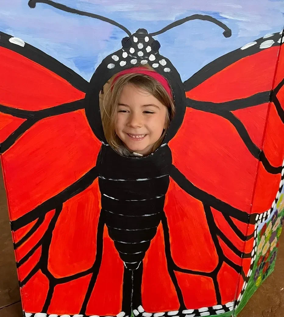 Child’s face framed in a painted red and black butterfly cutout