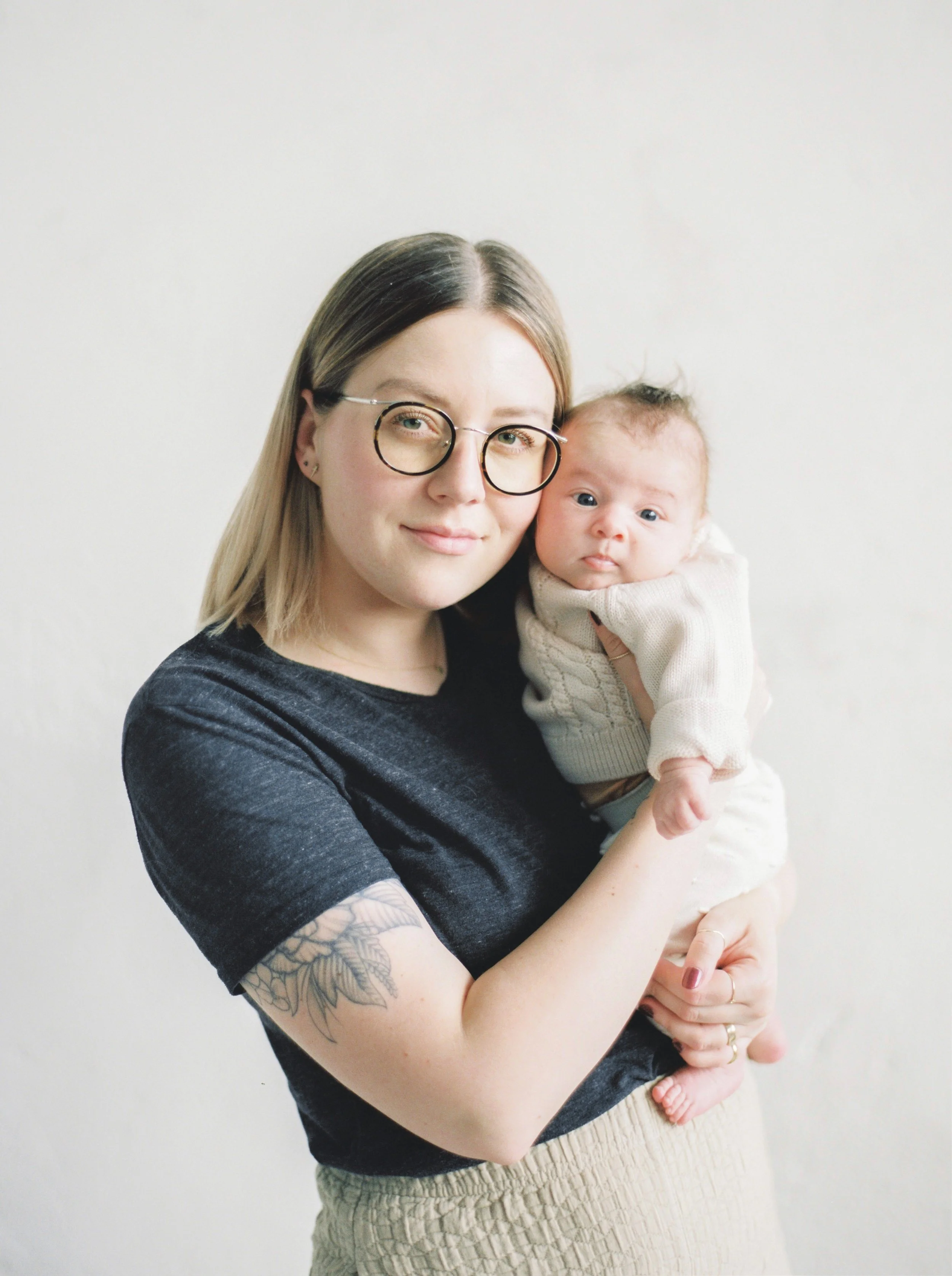 A woman with glasses holding a baby in front of a plain white wall at a Dartmouth family photography session. 
