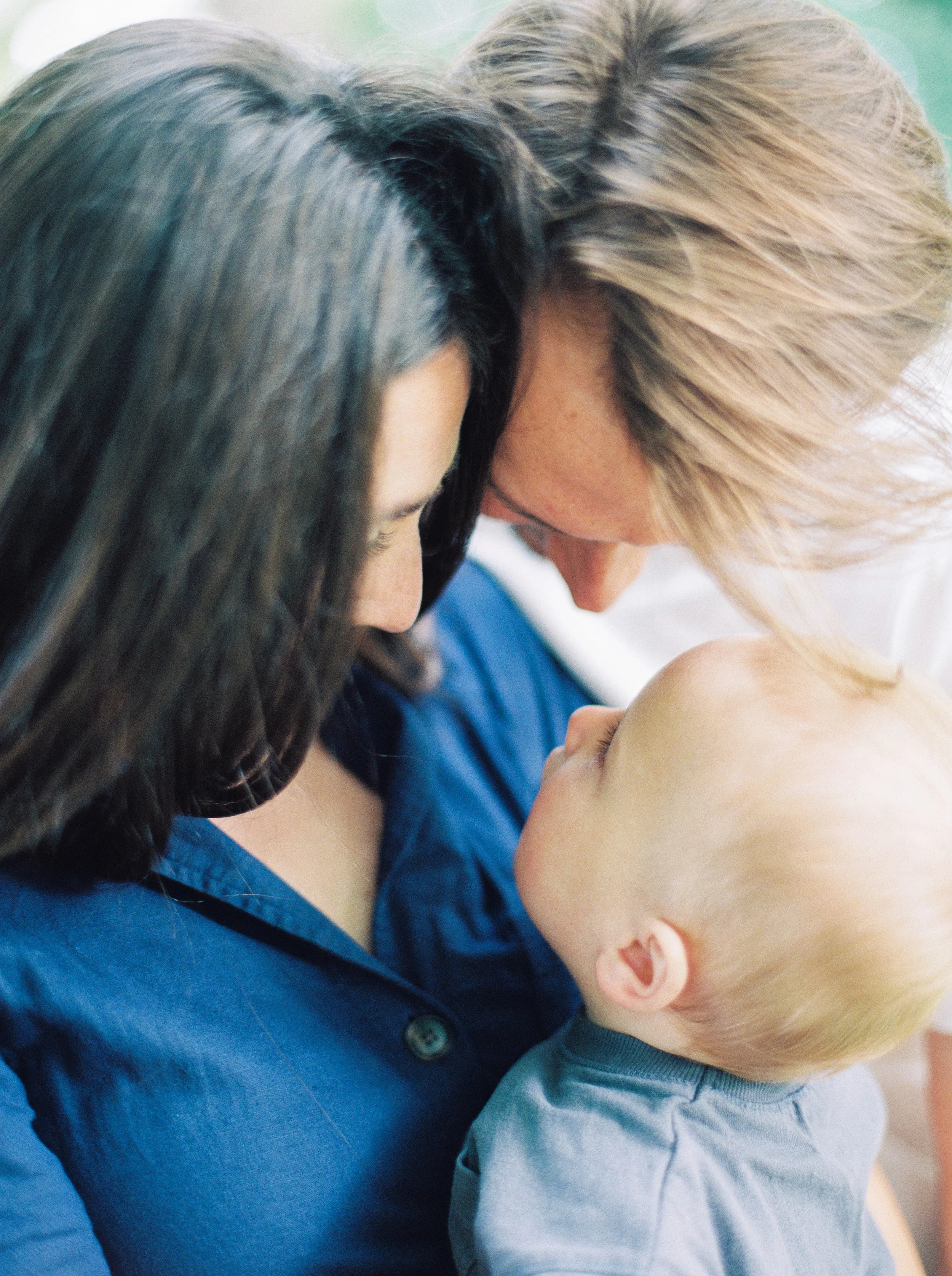 A woman with blonde hair and a young child with a bald head share a tender moment, with their foreheads touching, in a close-up shot at a Halifax family photography session. 