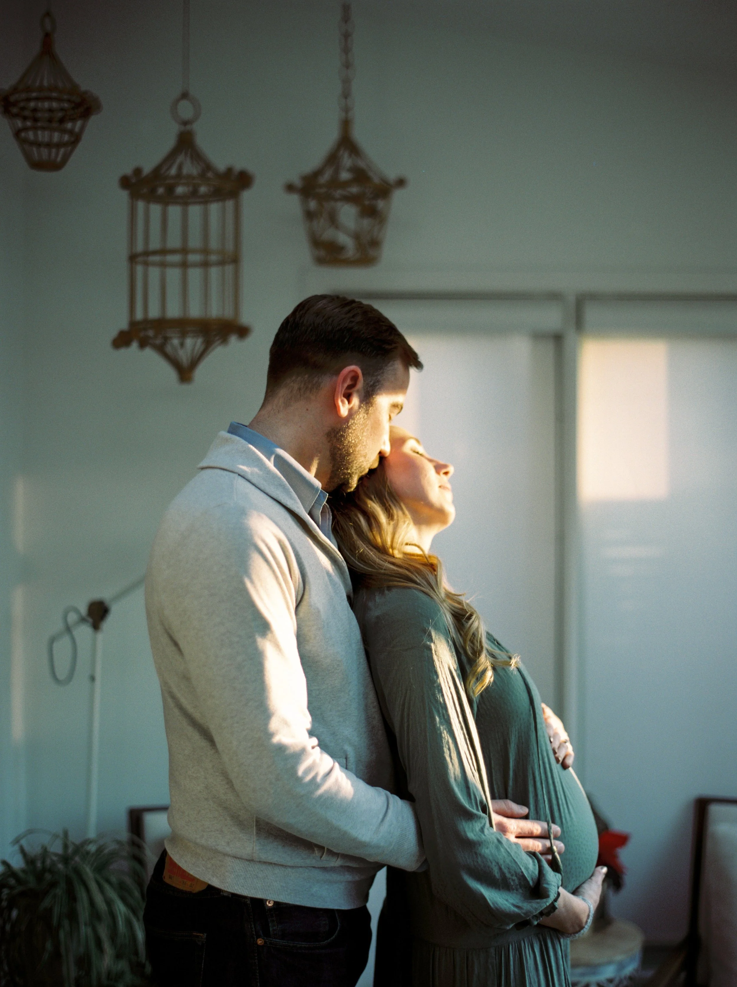 A man and a woman standing side by side with heads touching in a loving embrace, in a warmly lit room at a Halifax in home family session. 
