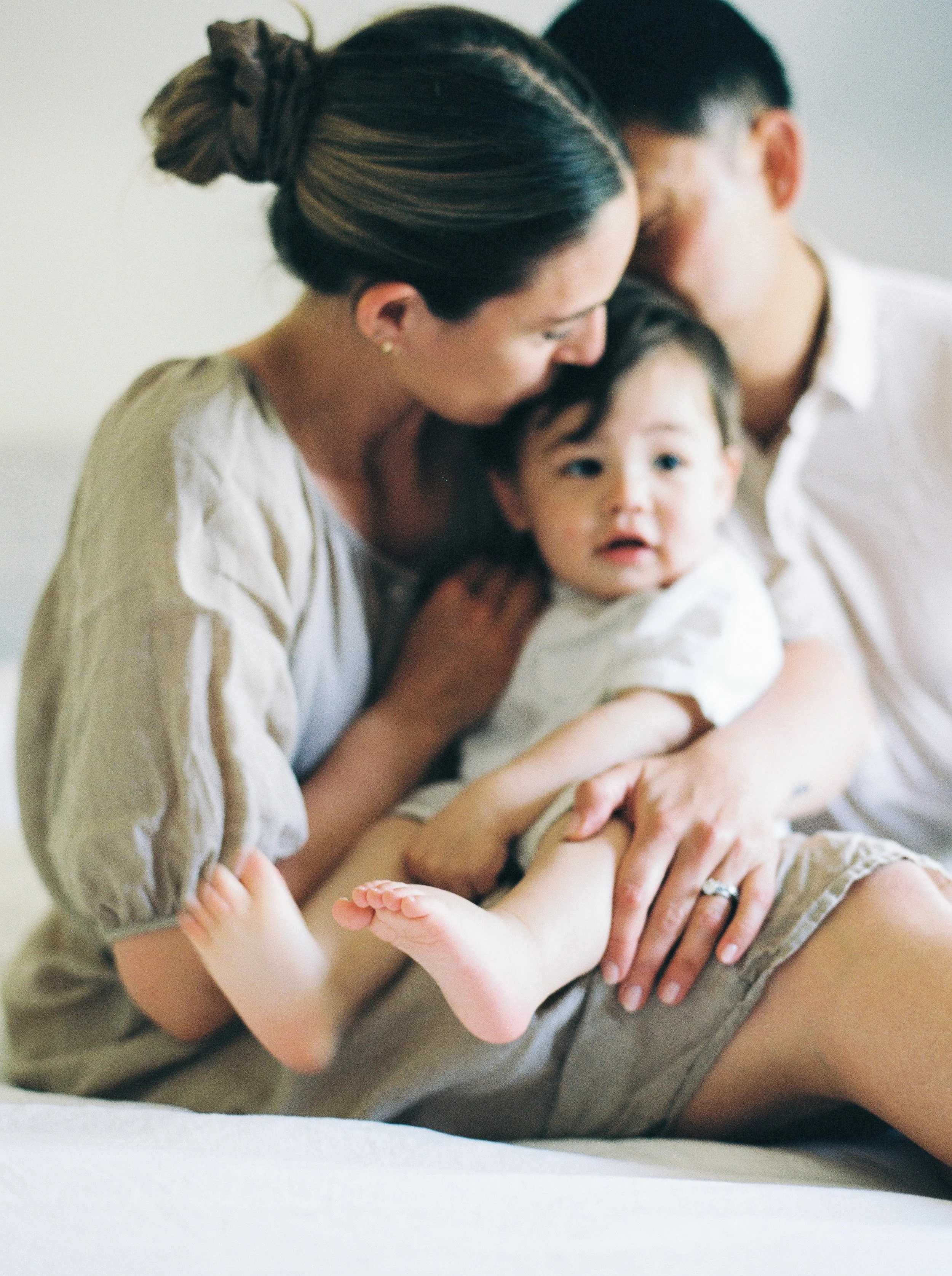 A woman, a man, and a young girl share an intimate moment, with the woman and man leaning in to kiss the girl on her cheeks, all three with eyes closed or looking down, creating a warm and loving scene Halifax in home family photography session.