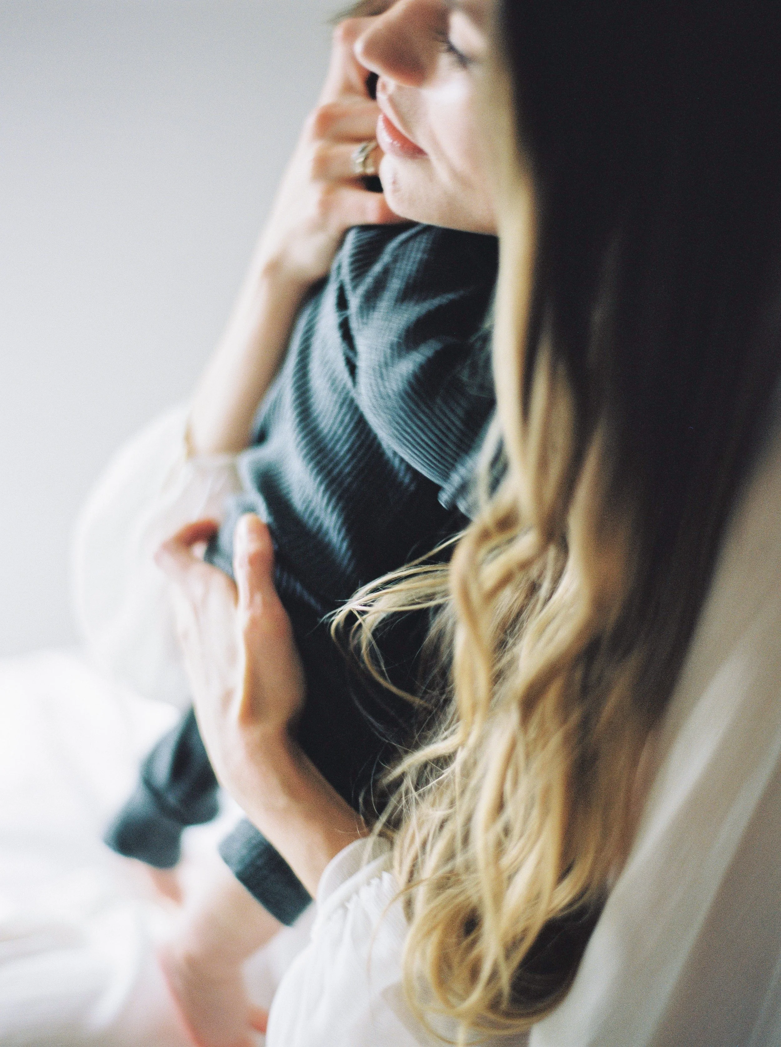 Close-up of a woman with long, wavy blonde hair resting her head on a white pillow, with her hand touching her face, wearing a black and white top at a Lawrencetown family photography session