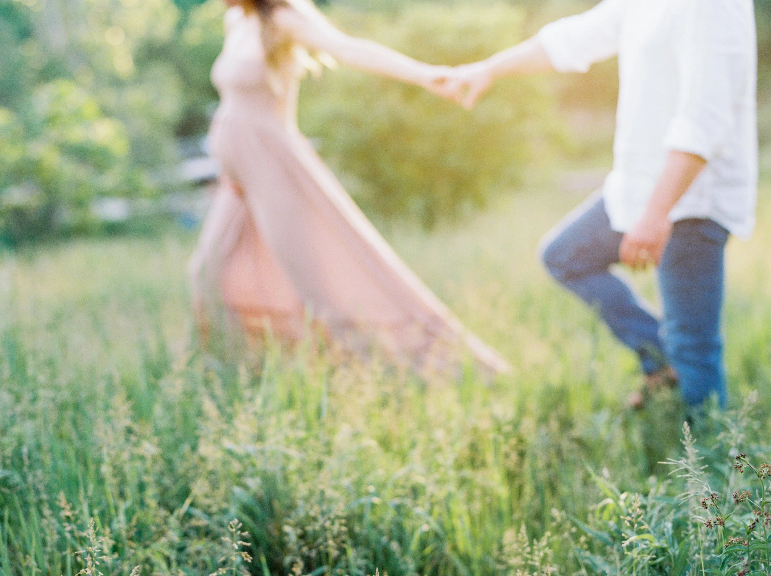 A person holding a young girl’s hand while walking through a grassy field with green trees in the background during daytime at a Dartmouth Maternity Photography session. 