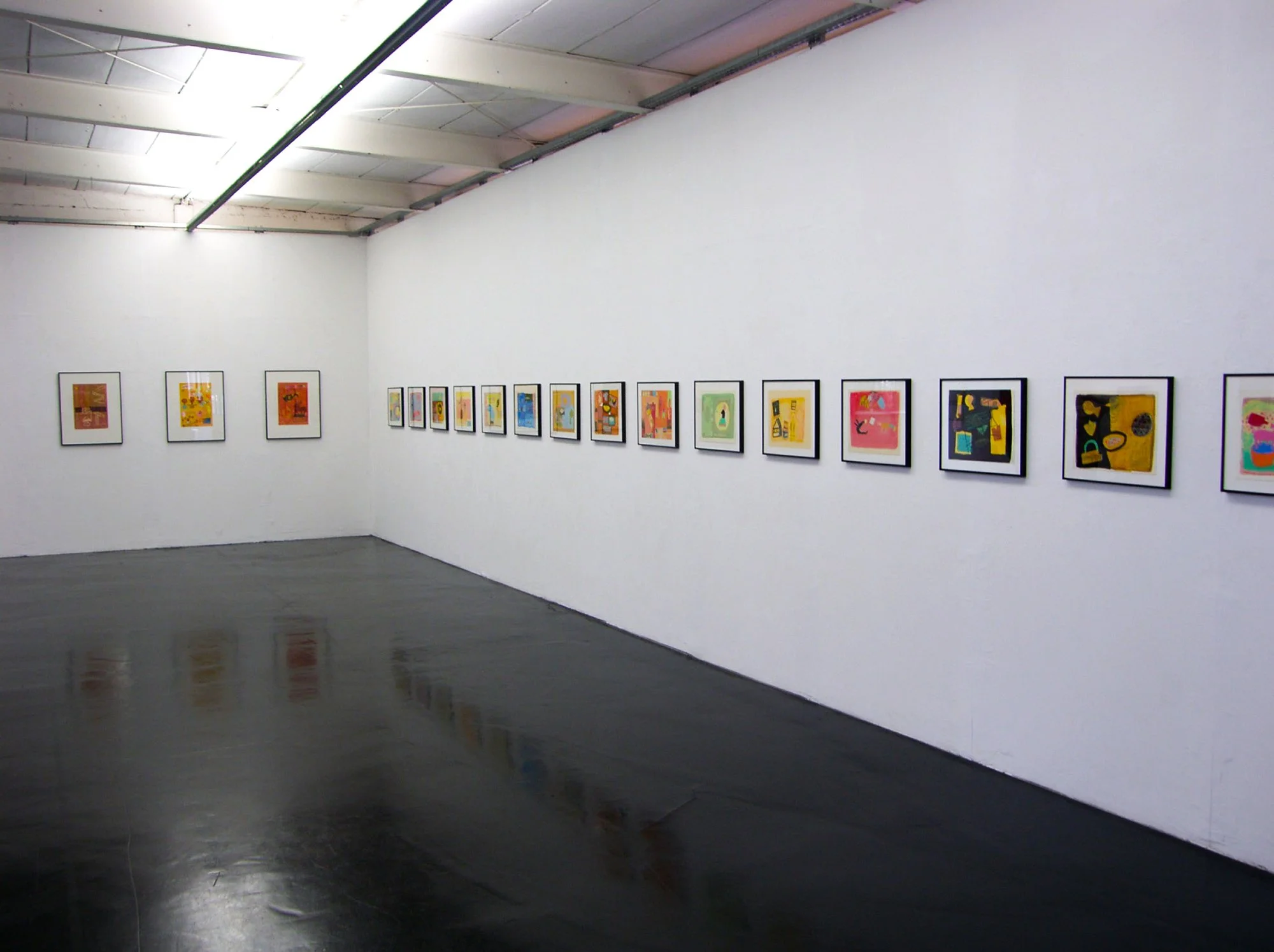 Photo of an art gallery wall displaying colorful abstract paintings, with a dark reflective floor and a white ceiling with exposed beams.