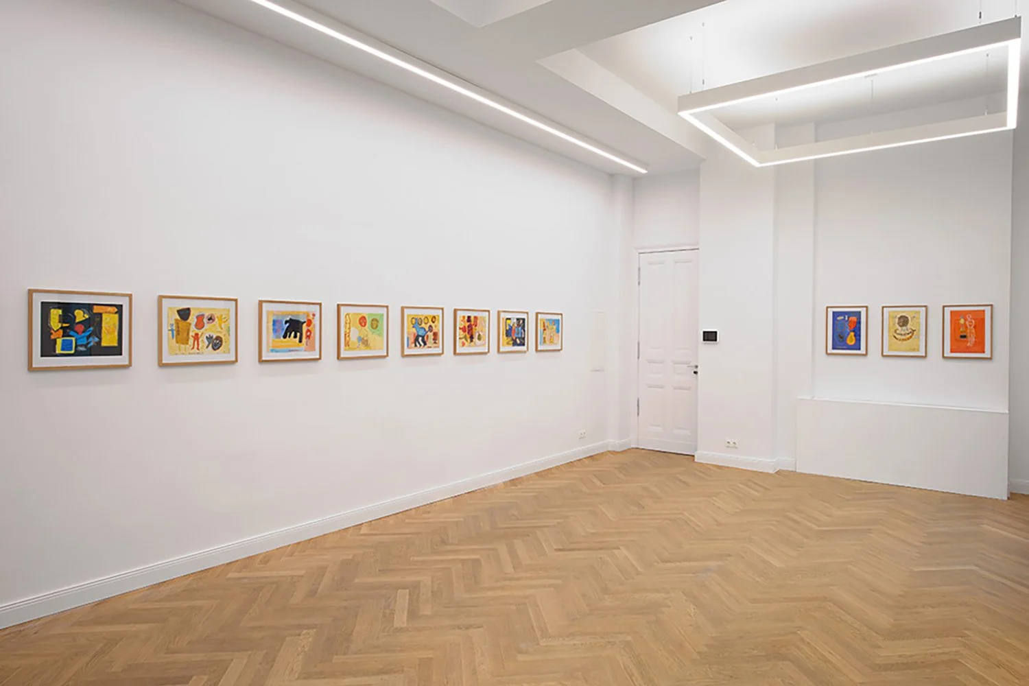 Art gallery with framed colorful abstract paintings on white walls, wooden herringbone floor, contemporary lighting fixtures.