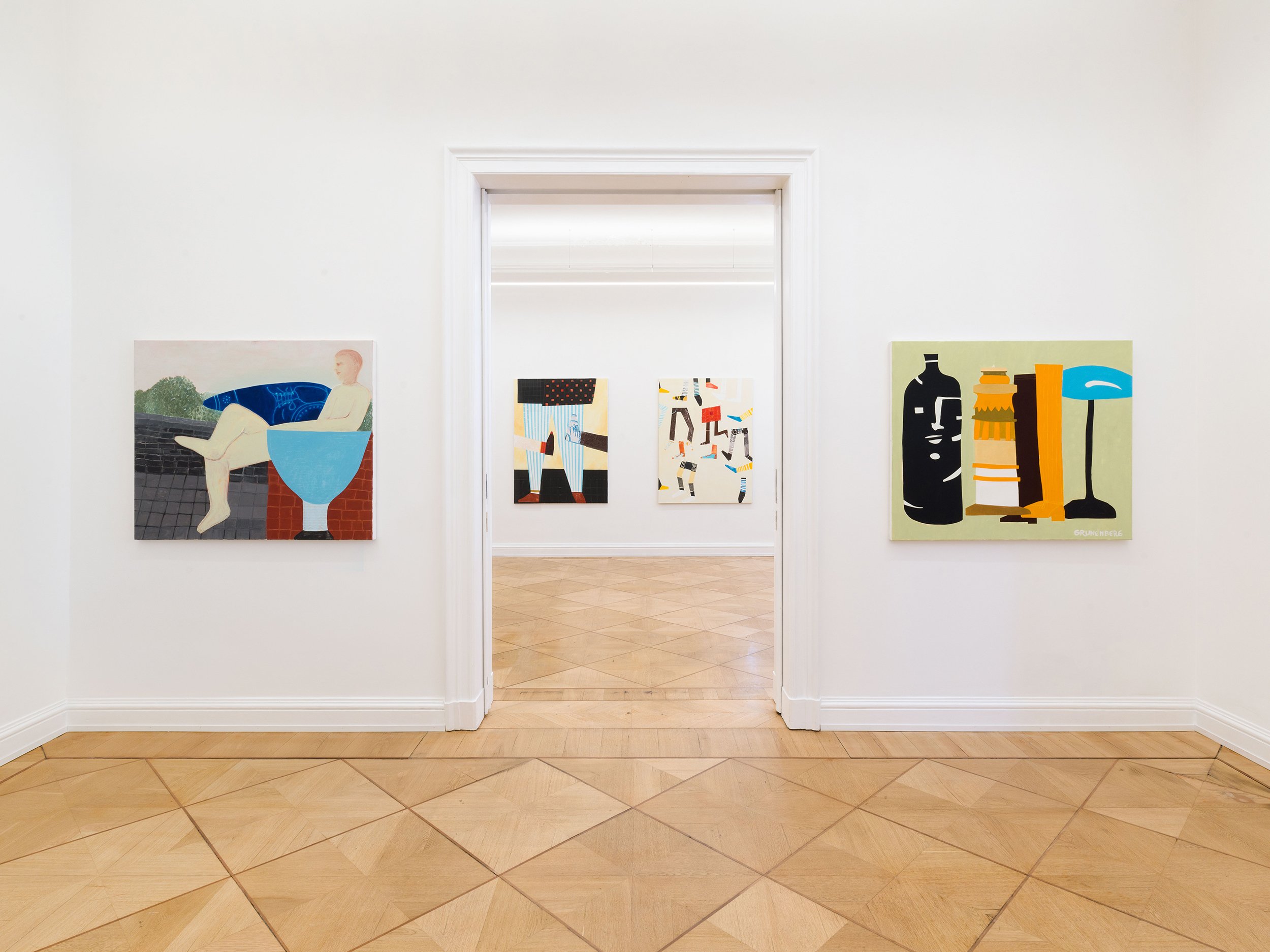 View of an art gallery with paintings on white walls, seen through doorways with wood flooring.