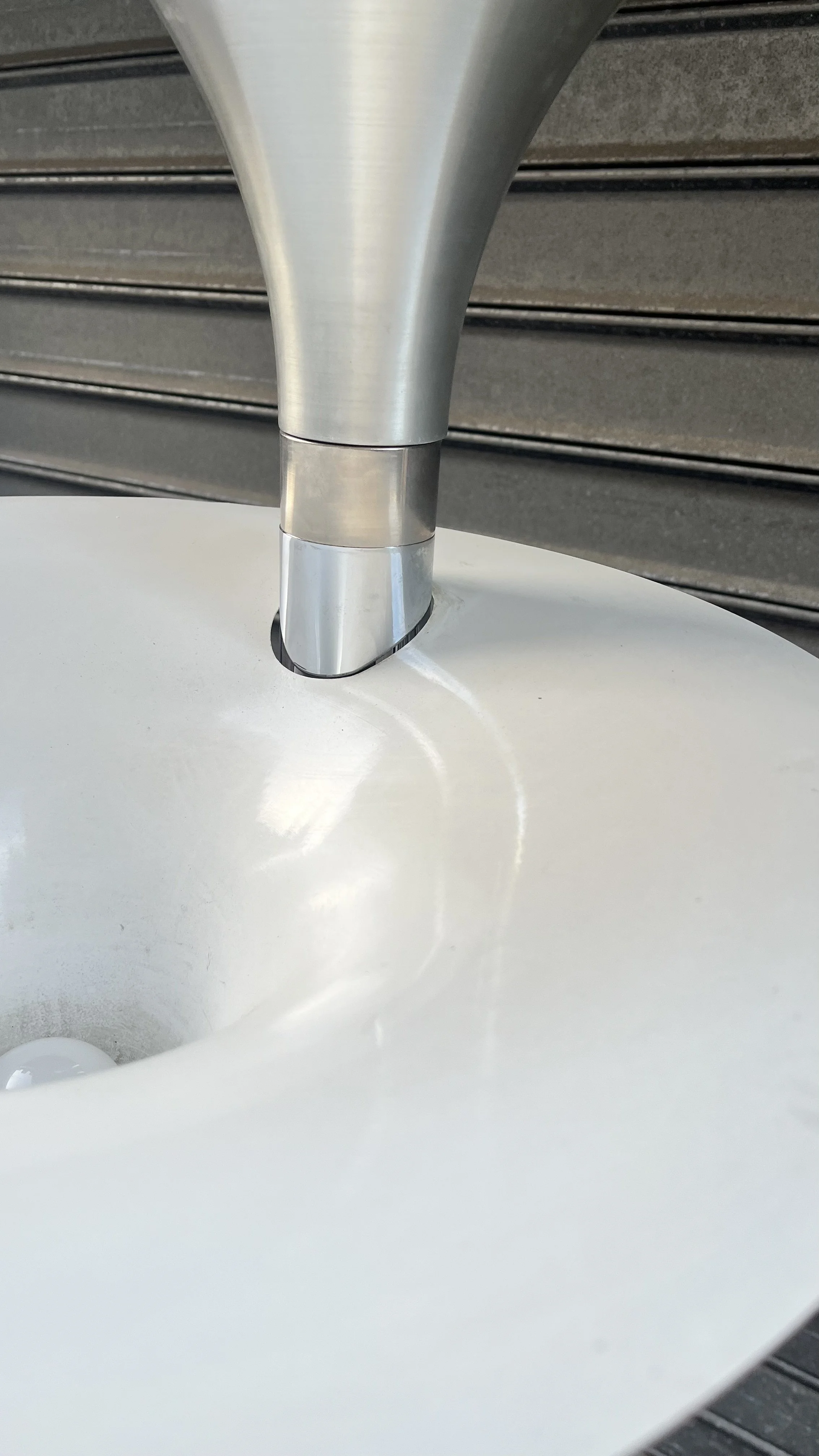 Détail d’une vasque en aluminium brossé à l’intérieur laqué blanc, avec le fût chromé qui la traverse