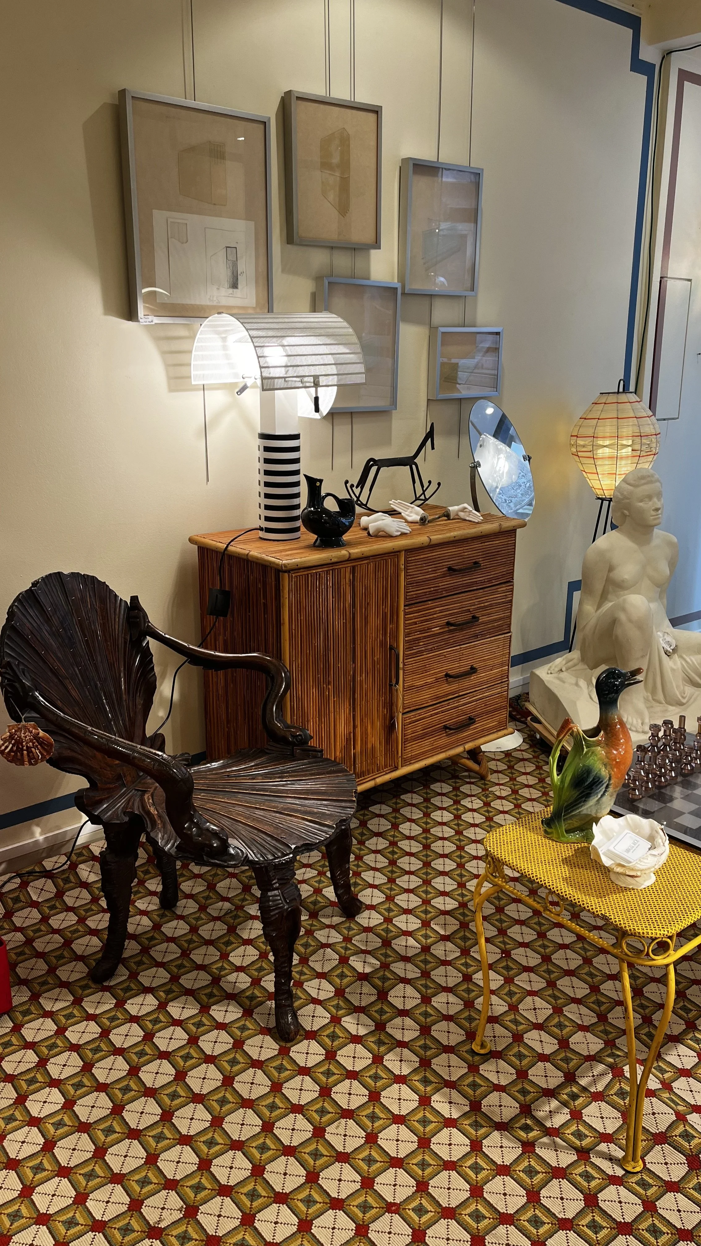 Vu intérieur boutique Ambroise ALLIOU avec meuble en osier et rotin, fauteuil dit "Grotto", lampe Mario Bellini et tableaux contemporains