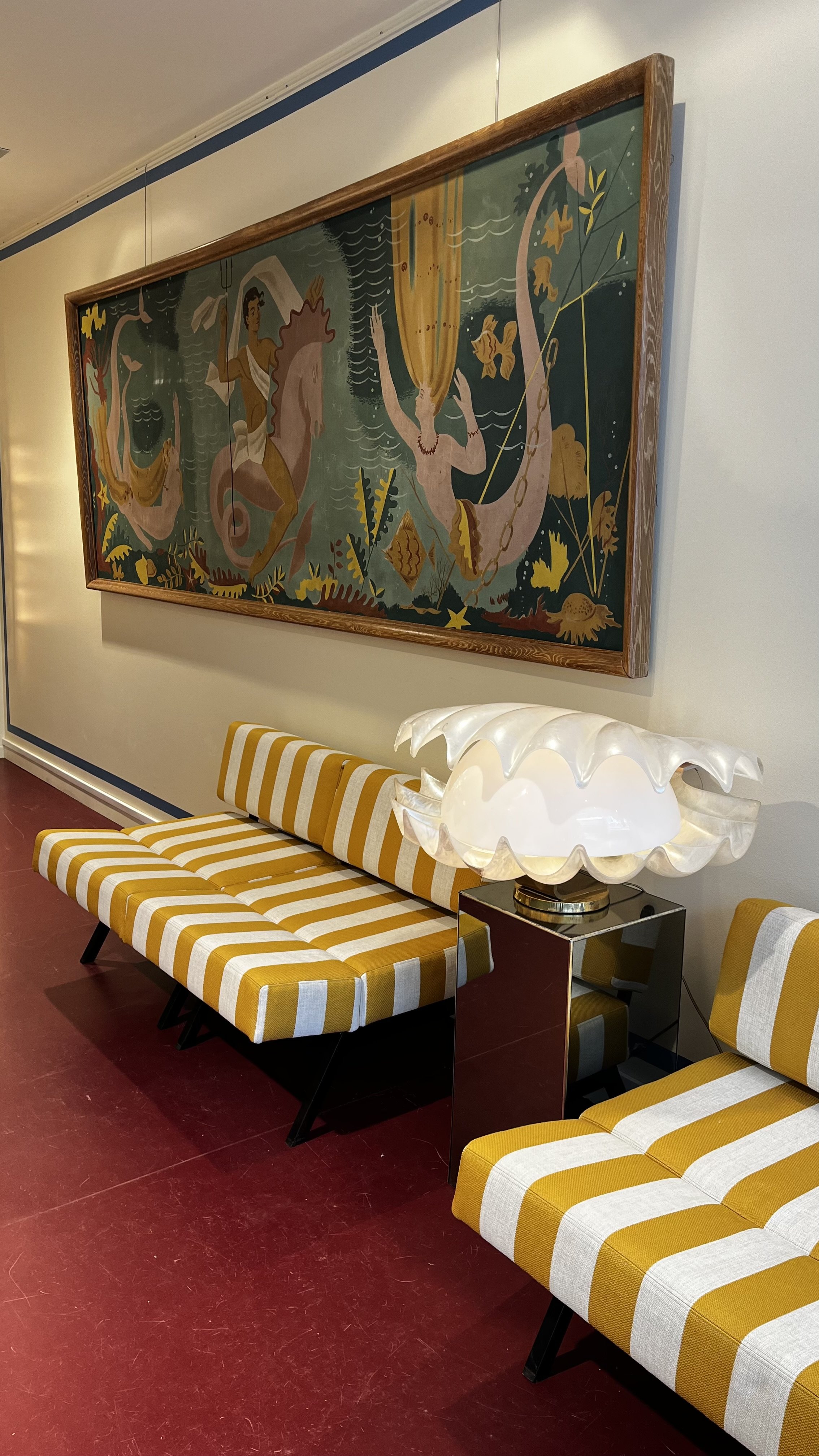 Vu de l'intérieur de la boutique Ambroise ALLIOU avec une suite de trois chauffeuses de Rito Valla pour I.P.E. Bologna, modèle "Panchetto". Arrière fond une grande huile sur toile avec sirènes des années 60