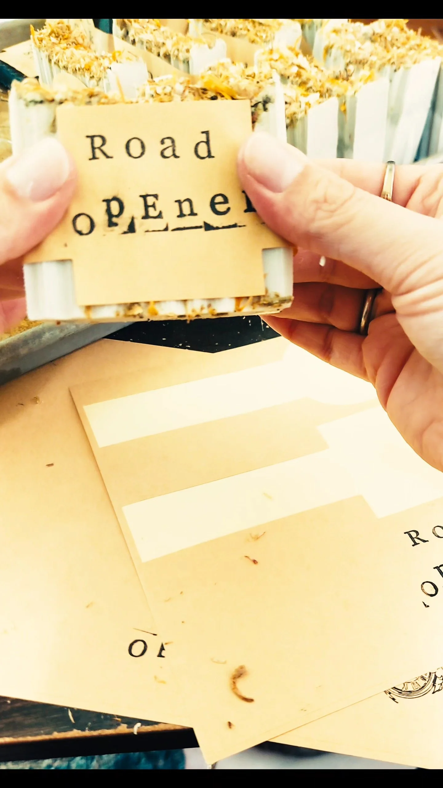 Person holding a yellow paper label with stenciled black text that reads "Road Open" in front of a box of matches.