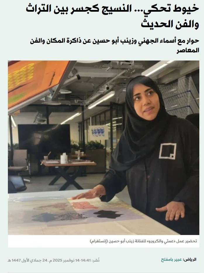Woman in black hijab and black shirt standing at a table, working on a large printed map or artwork. The background shows a modern office or workspace with glass walls, tables, and a TV screen. Arabic text at the top and bottom describes the scene, m