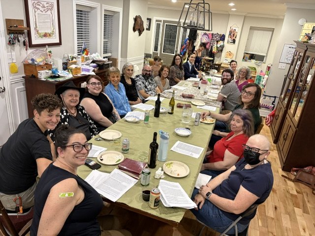 A group of people sitting around a long dining table in a home, celebrating together with food and drinks.