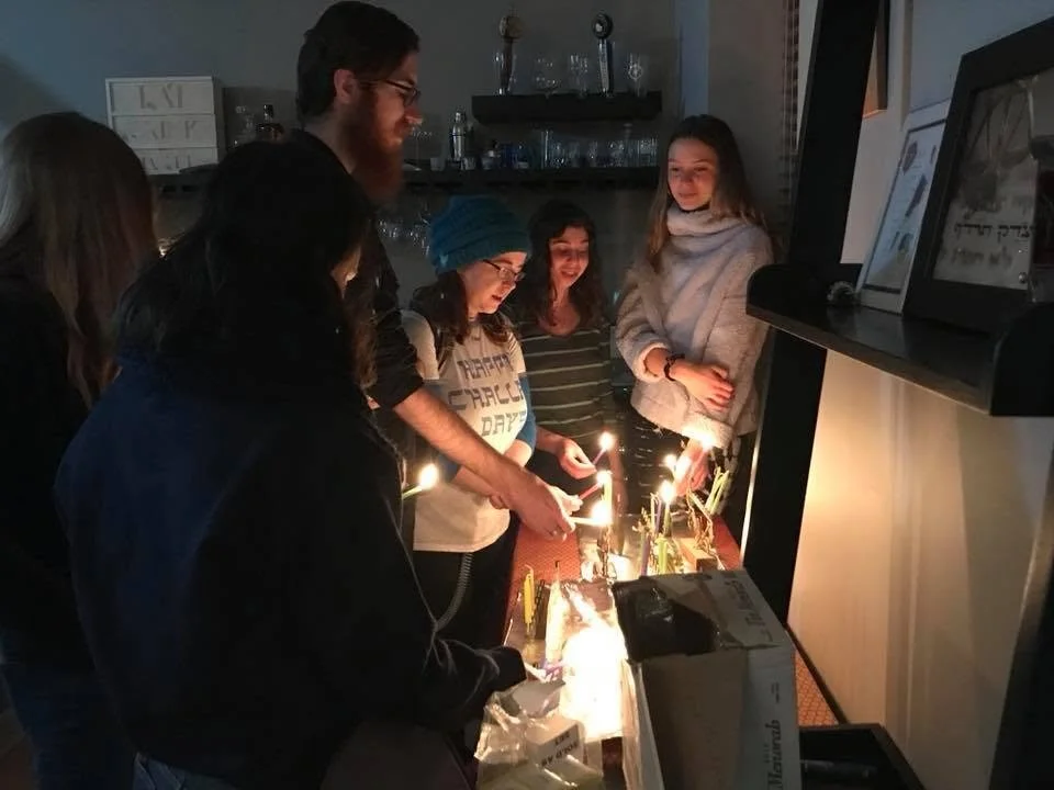 Group of people celebrating with birthday candles on a cake in a dimly lit room.
