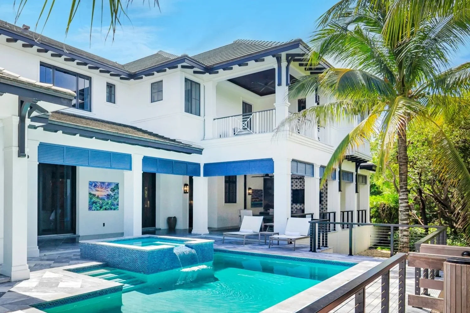 Luxury two-story house with a backyard pool, palm trees, and outdoor seating area under blue skies.