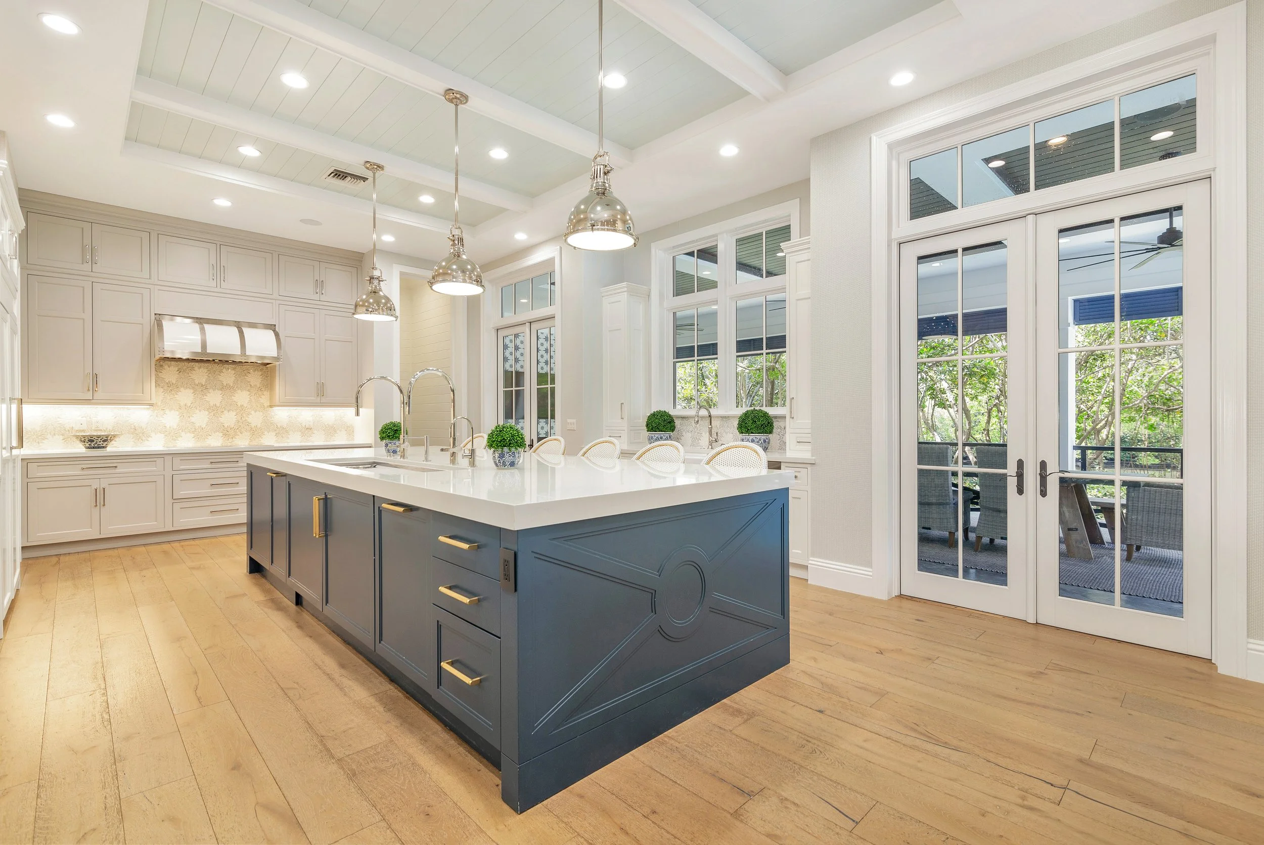 Modern kitchen with white upper cabinets and a dark blue island, large windows, and a sliding glass door leading to an outdoor patio with seating.