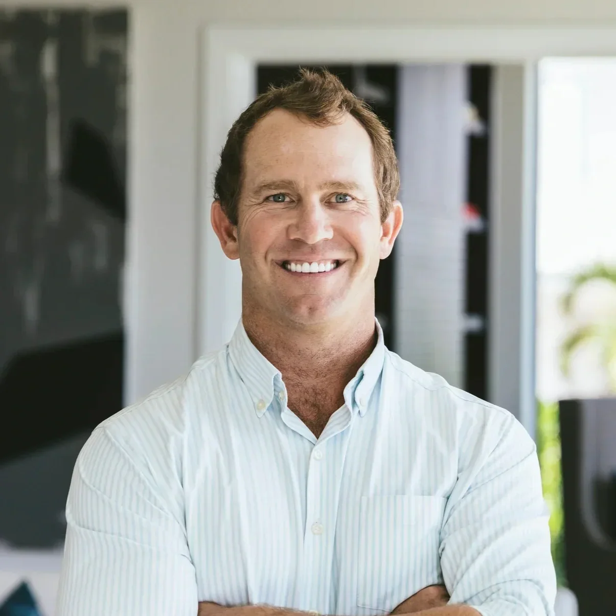 A smiling man with light brown hair in a collared shirt standing indoors.