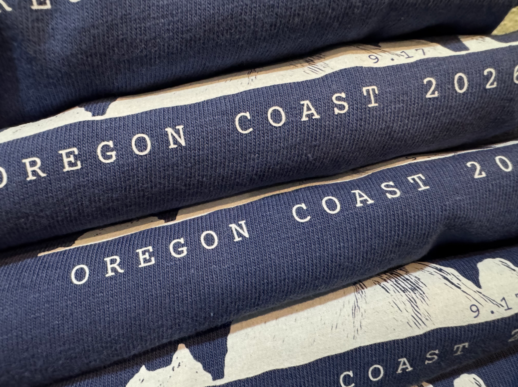 Close-up of blue fabric with white text reading "Oregon Coast 2020" repeated on several stacked layers.