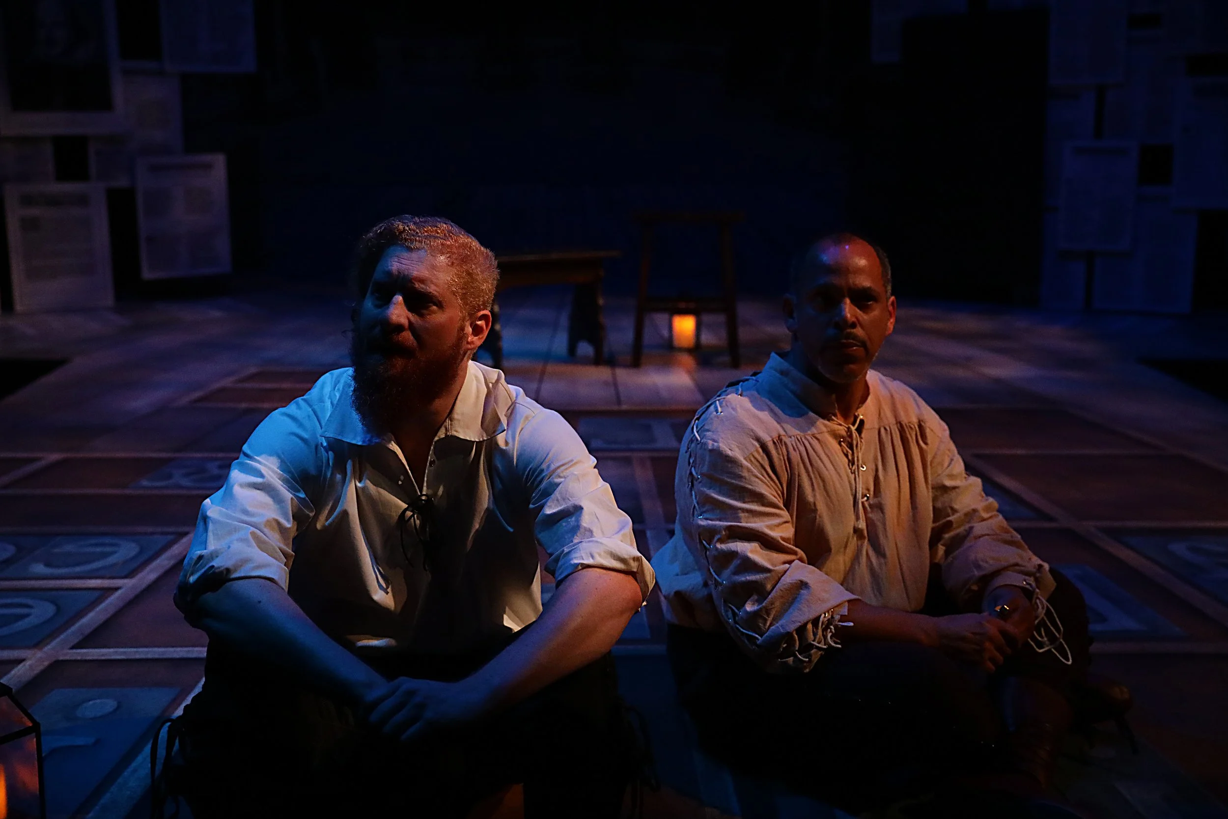 Book Of Will Production Photo: Two men sitting in the dark with a lantern casting a soft warm glow