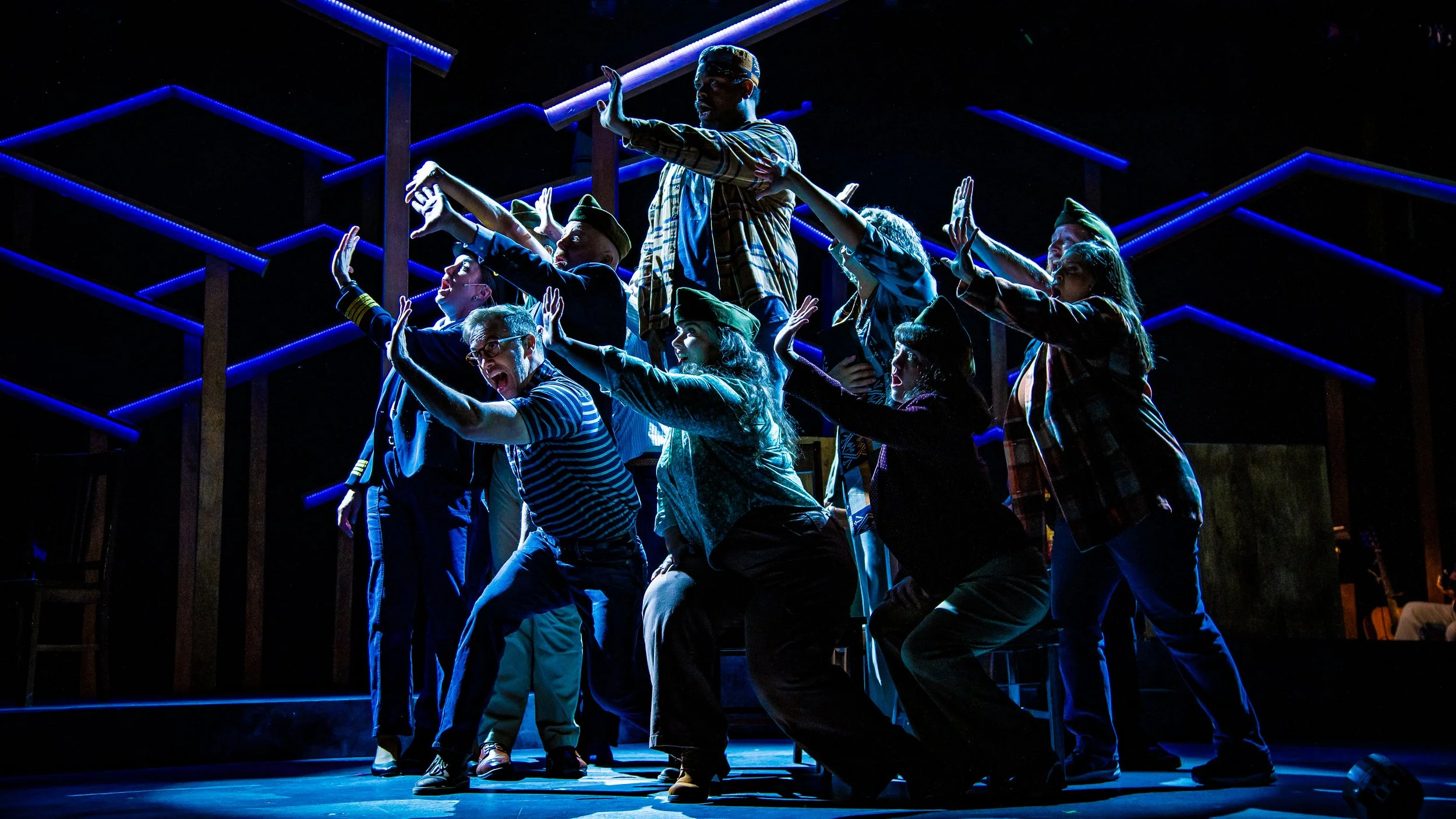 Come From Away Production Photo: A group of people outstretching an arm and highlighted in backlight