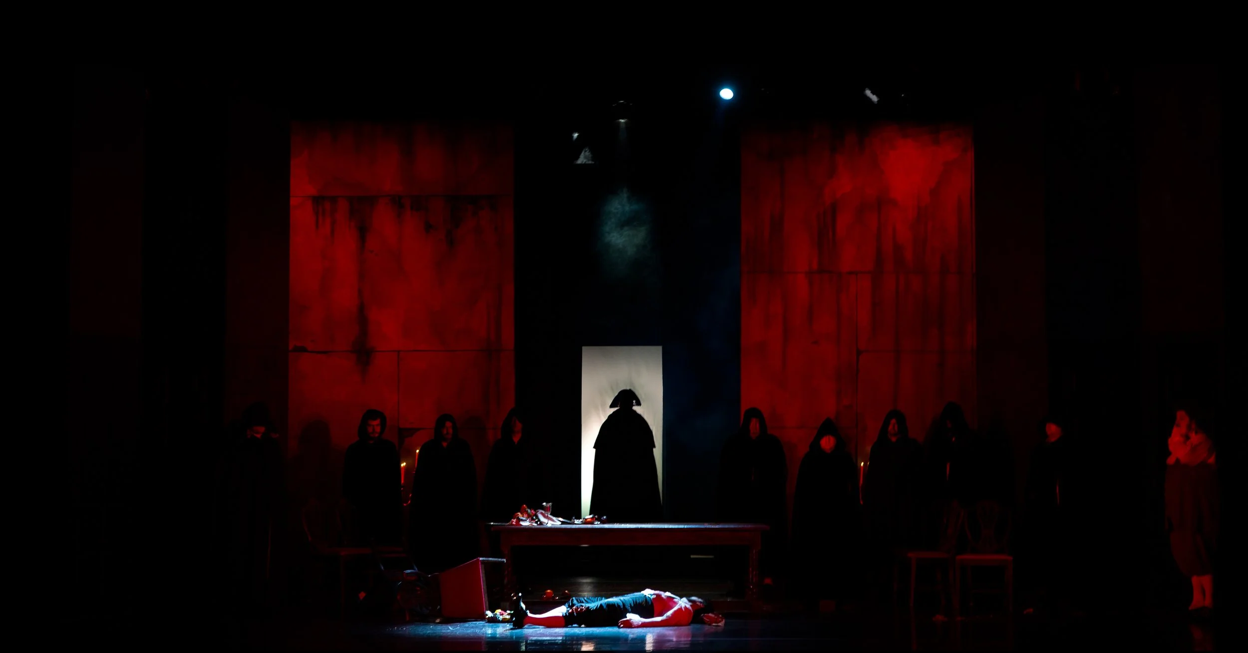 Don Giovanni Production Photo of a hooded figure silhouetted in white and surrounded by deep red walls.