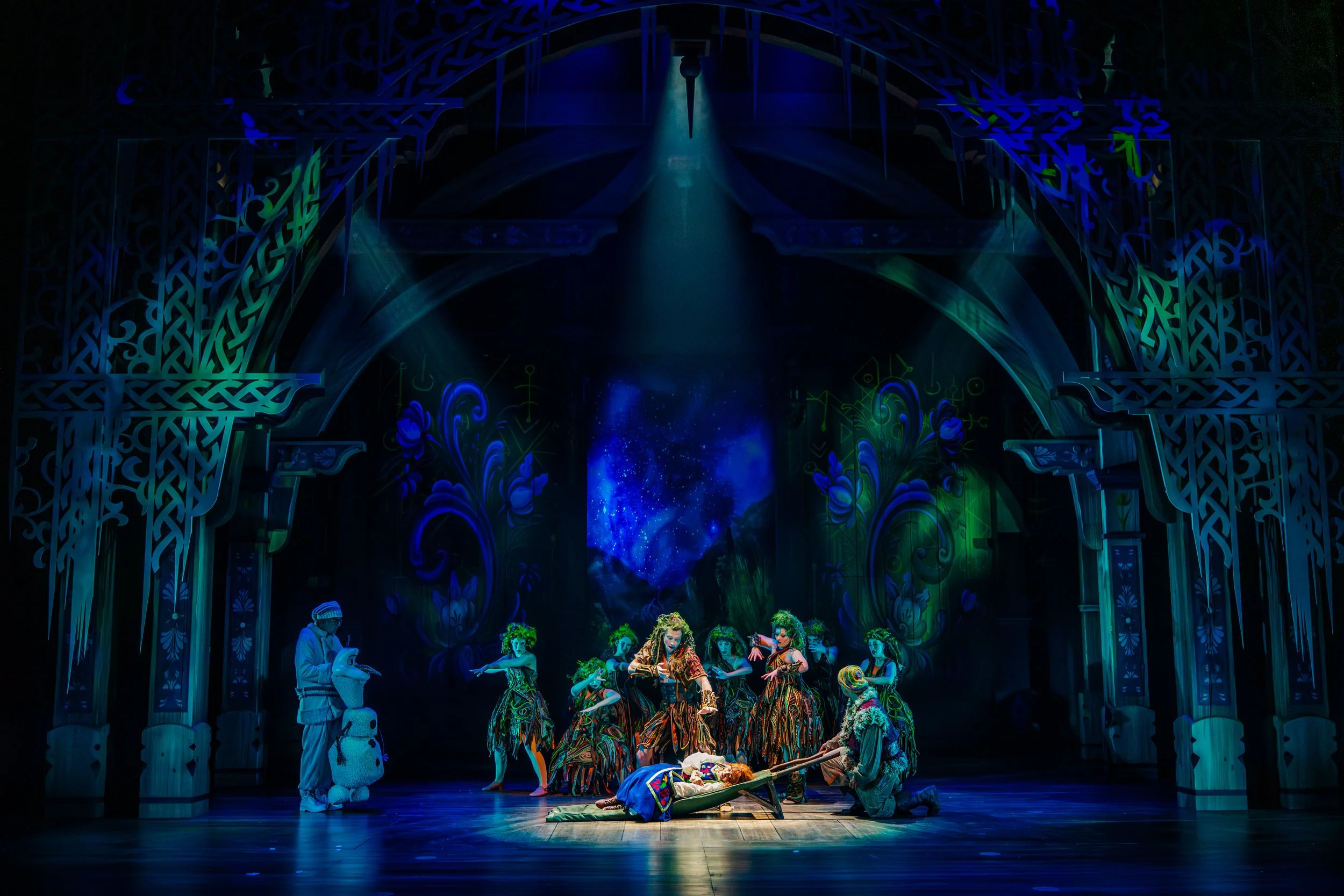 Frozen Production Photo: A group of hidden folk highlighting Anna on the floor with a background of blue, green, and purples