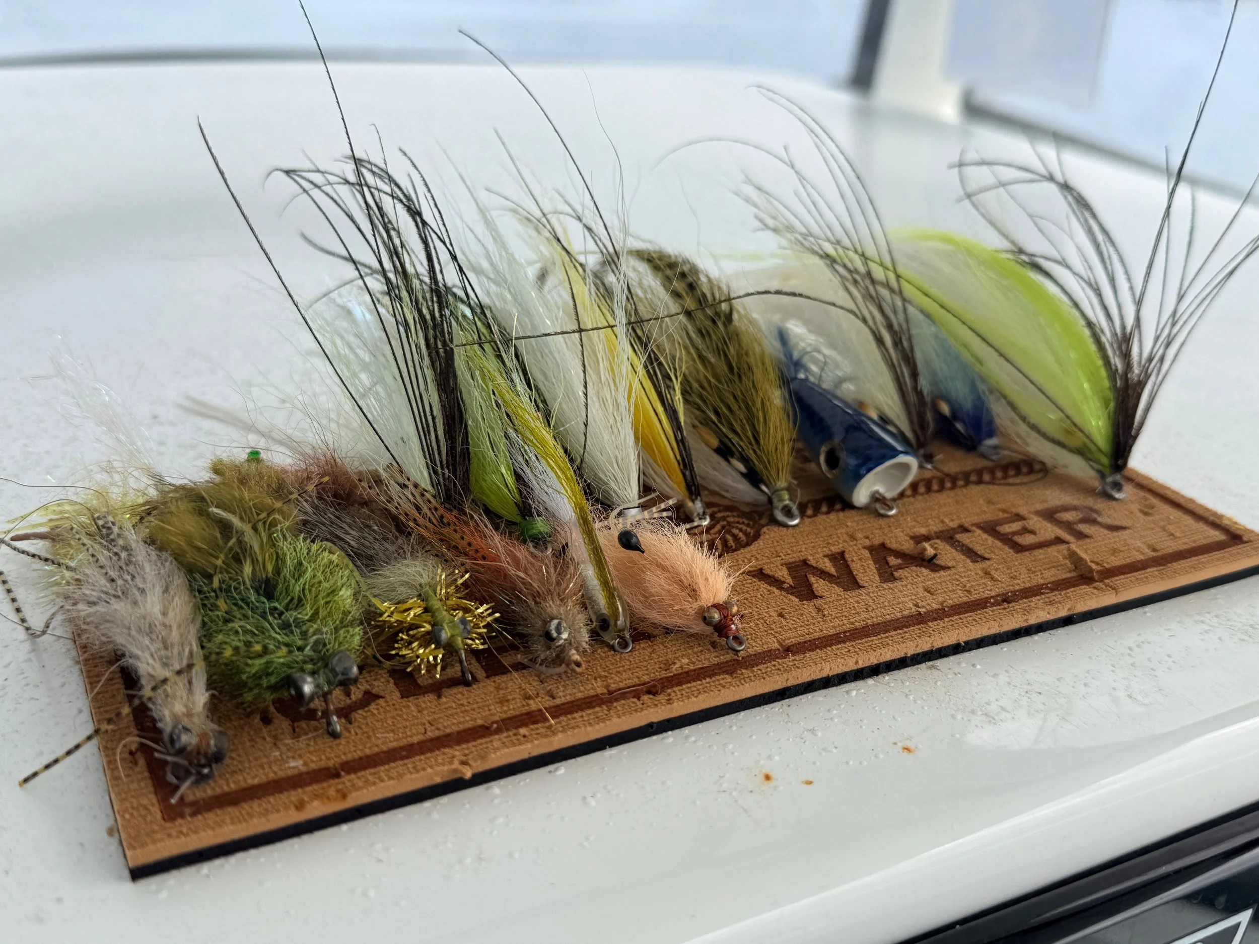A collection of fishing lures with feathered and plastic bodies, arranged on a wooden display board.